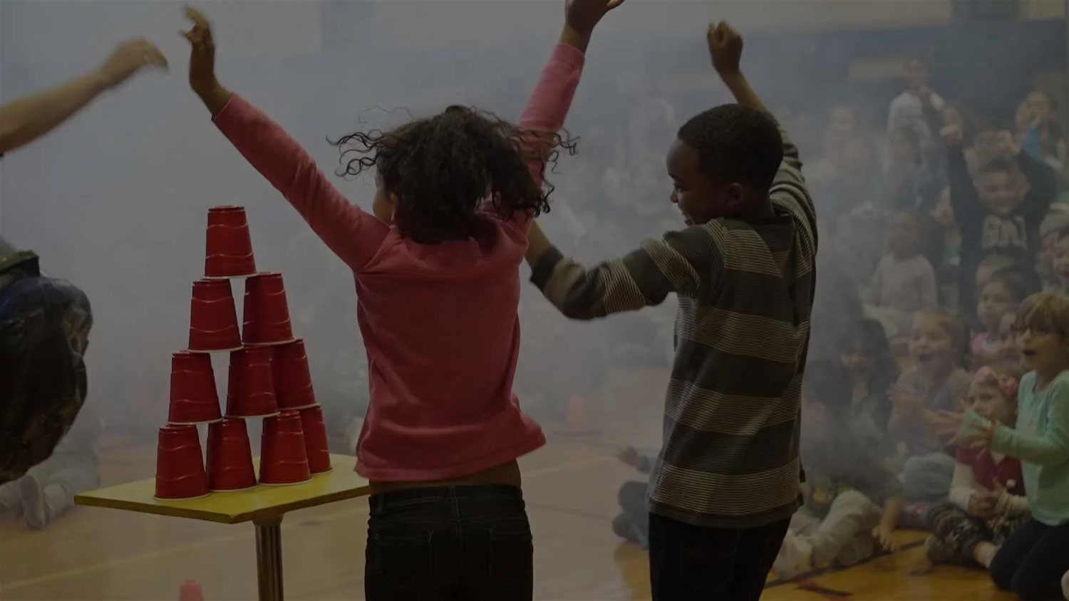 Elementary students jumping as vortex rings knock over cup towers at a science assembly