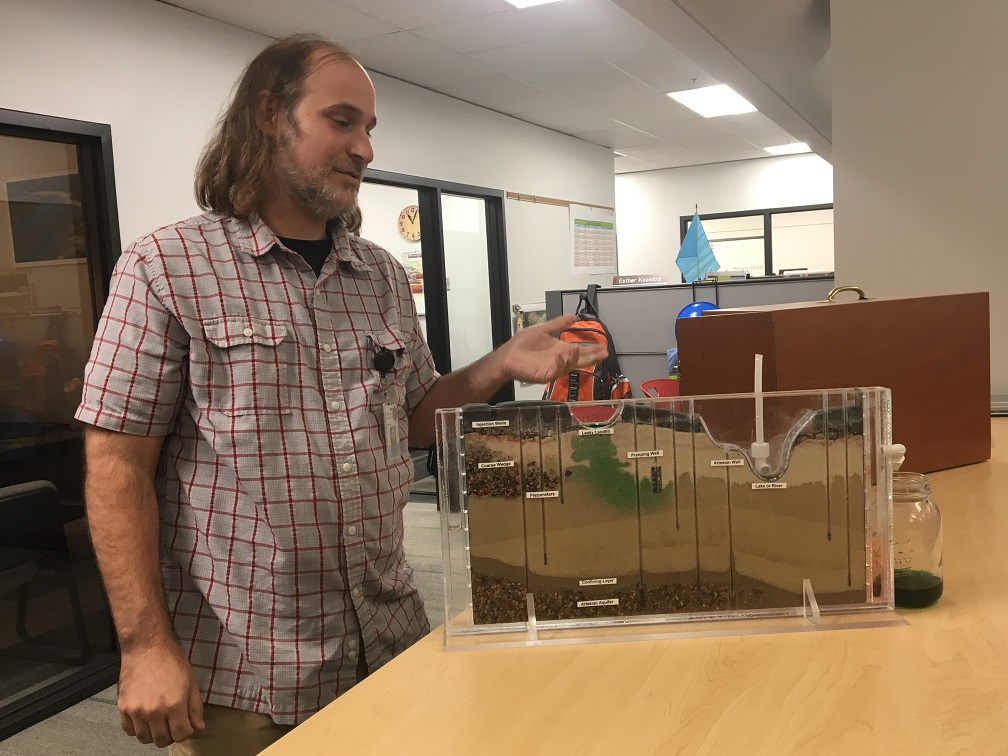  After Tom adds water to the left reservoir to simulate groundwater flow, you see the contamination start to spread to the right — toward the river. 