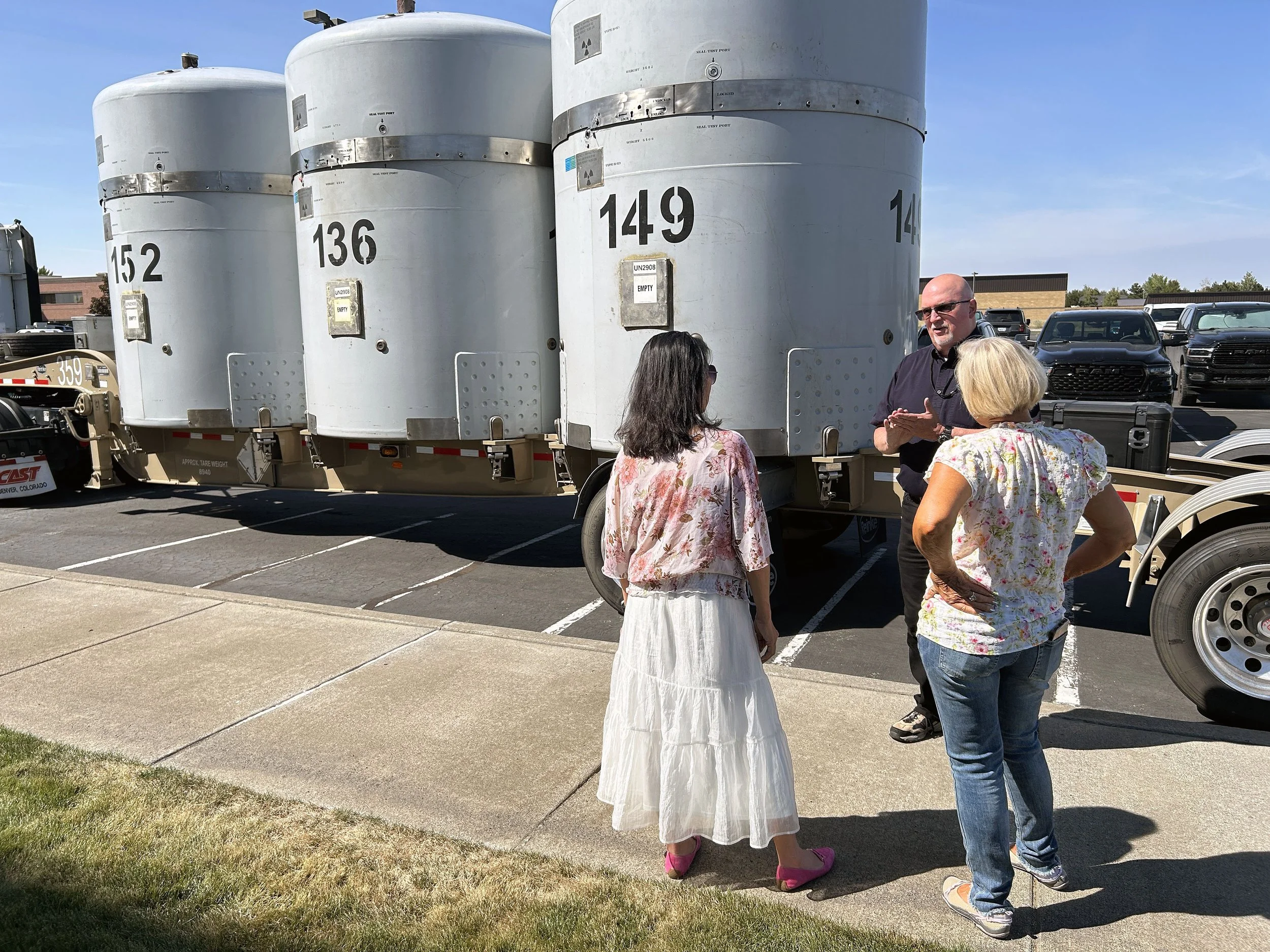 A man faces toward the camera, talking with his hands, as two woman face him with example TRU transport canisters in the background.
