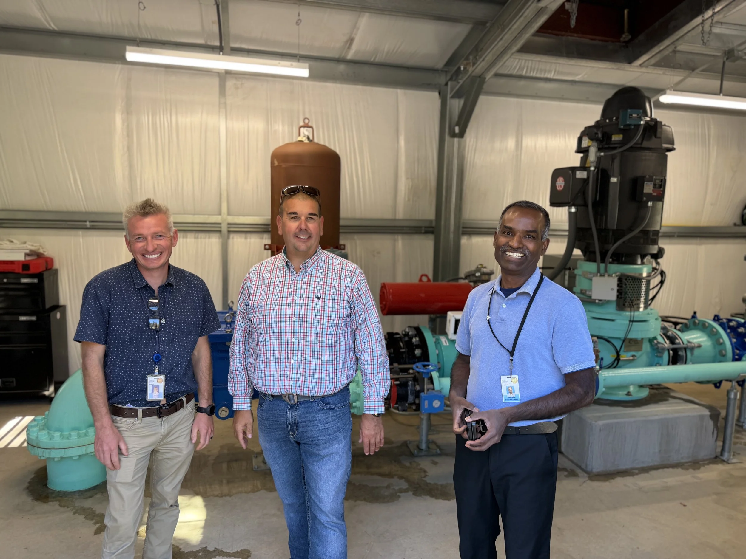 Three men smile for a photo inside the pump station.