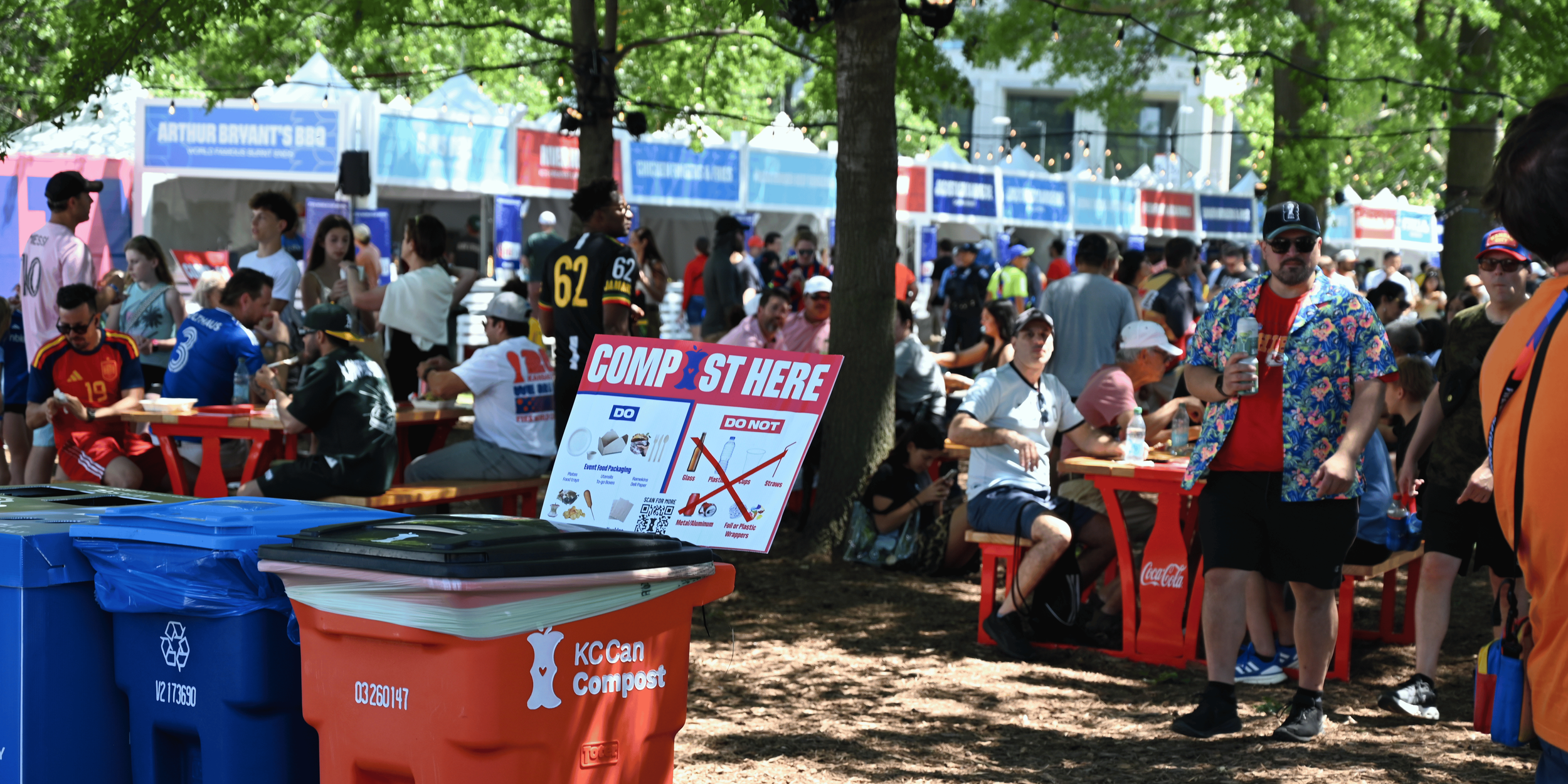 Fans at KC Fan Festival enjoying a bite to eat in the food court. Compost sign and can in foreground.