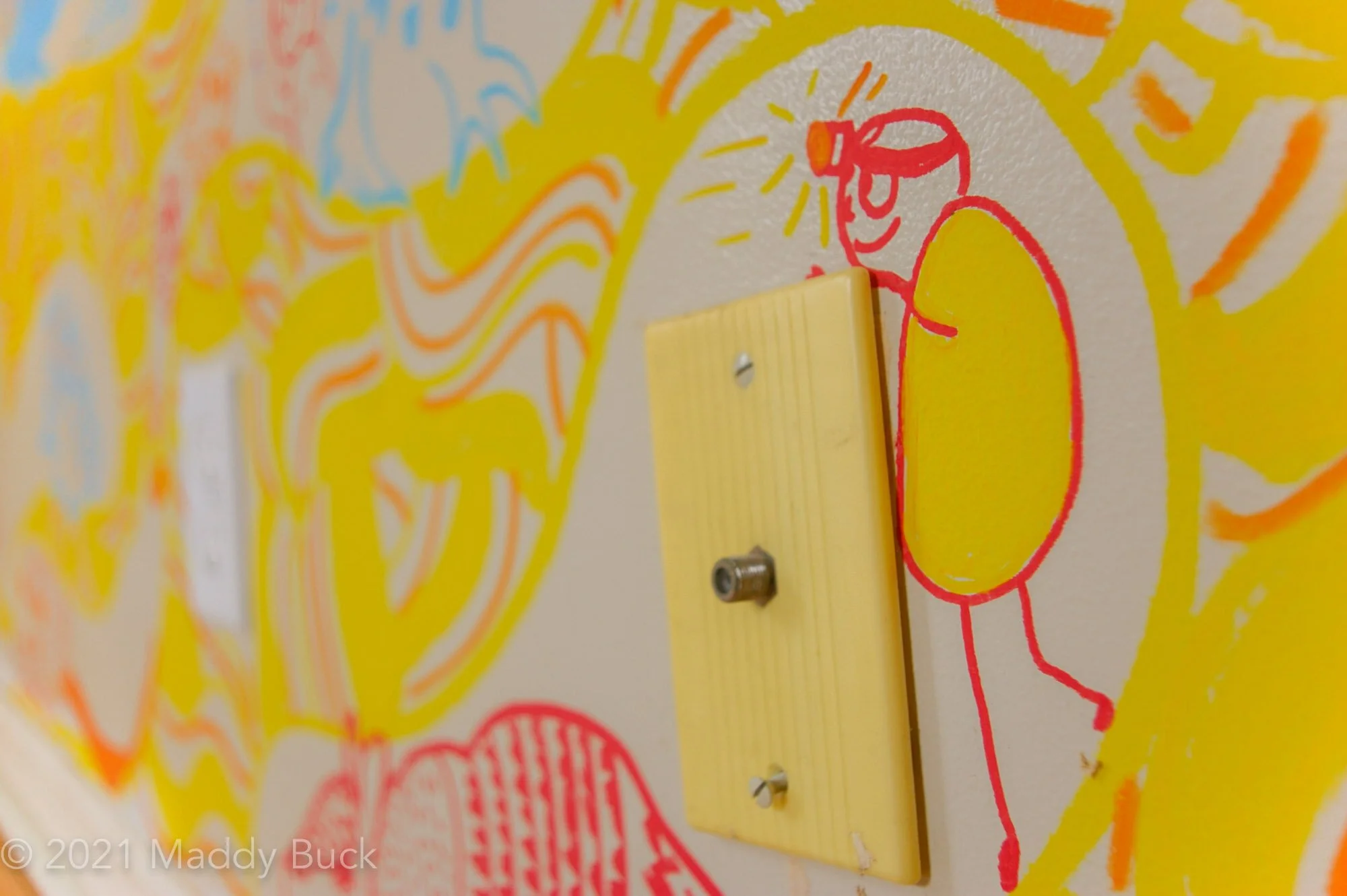  This is a close-up photograph of a mural in a kids’ bedroom. We see a little stick figure with a big yellow round body. The stick figure is an underground inspector. We see they have a headlamp on and are inspecting on top of the cable unit that is 