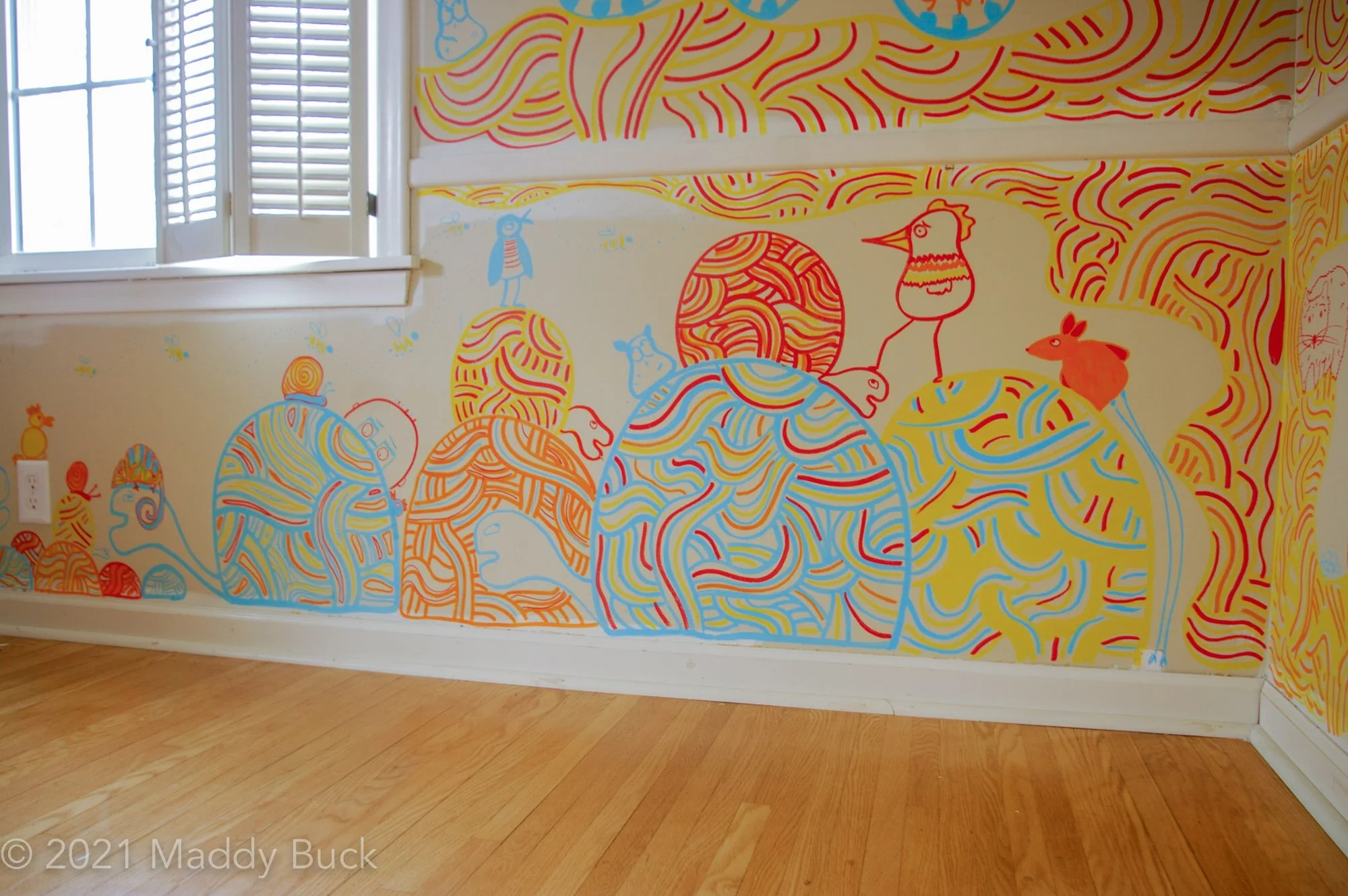  In this photo, we see the bottom of a mural in a nursery. We see a bunch of rocks in swirly colors, but when we look close, it’s clear that they’re turtles. On top of the turtles are a few smaller animals, mostly birds. Some swirly patters take up t