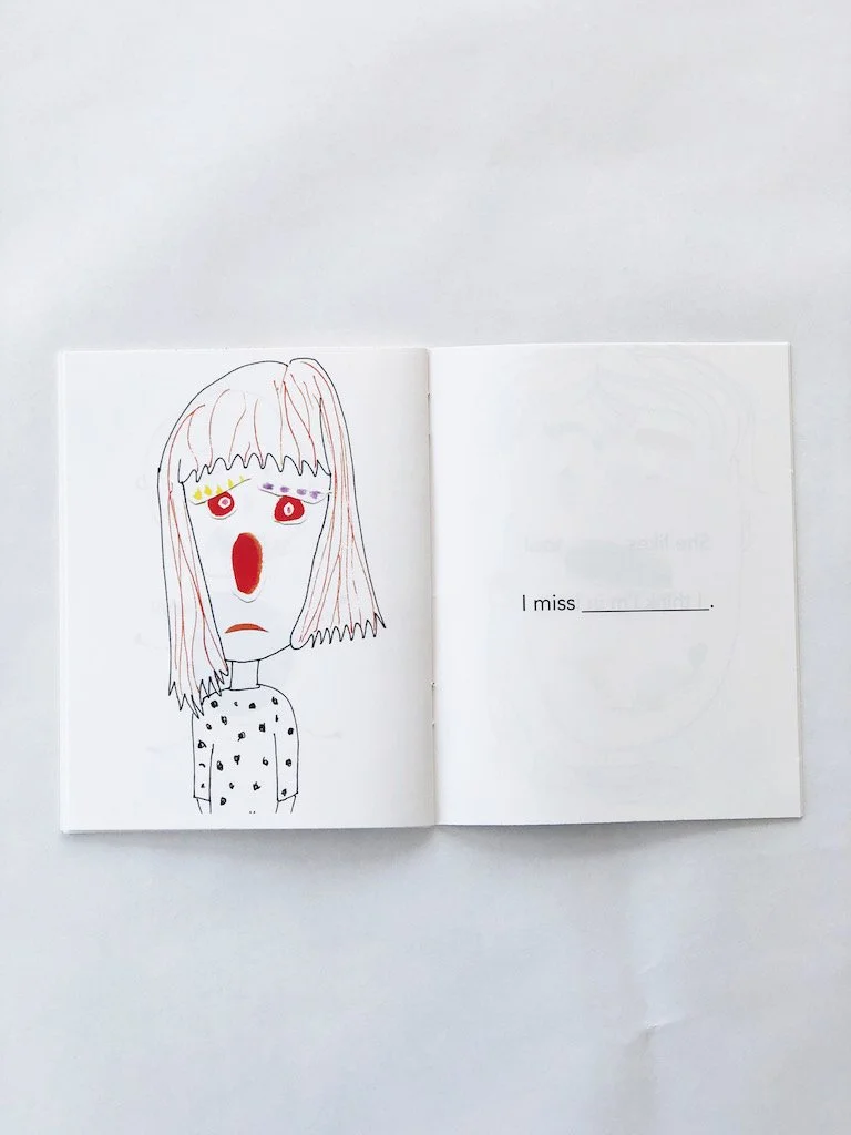  Photo of a picture book open to a page. On the left is a girl with a very sad looking face. Her eyes, nose, and mouth are created with collage pieces, blobs of watercolor paper that have been painted. On the right page is a sentence that says, “I mi