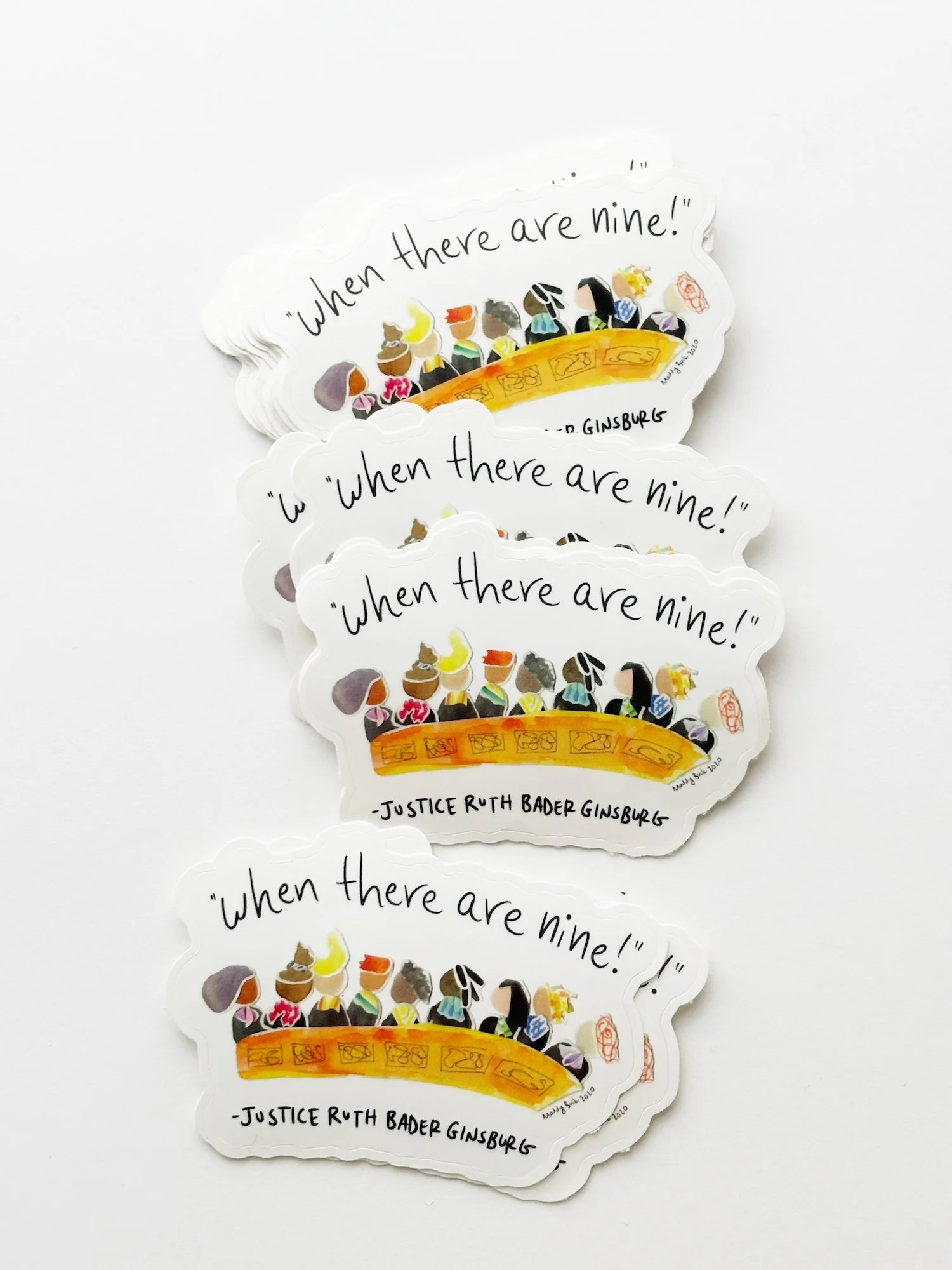  This is a photo of a pile of “When there are nine” stickers, which show a possible U.S. Supreme Court, where all nine members are women. The stickers are set on a white background and cascade across the page.  