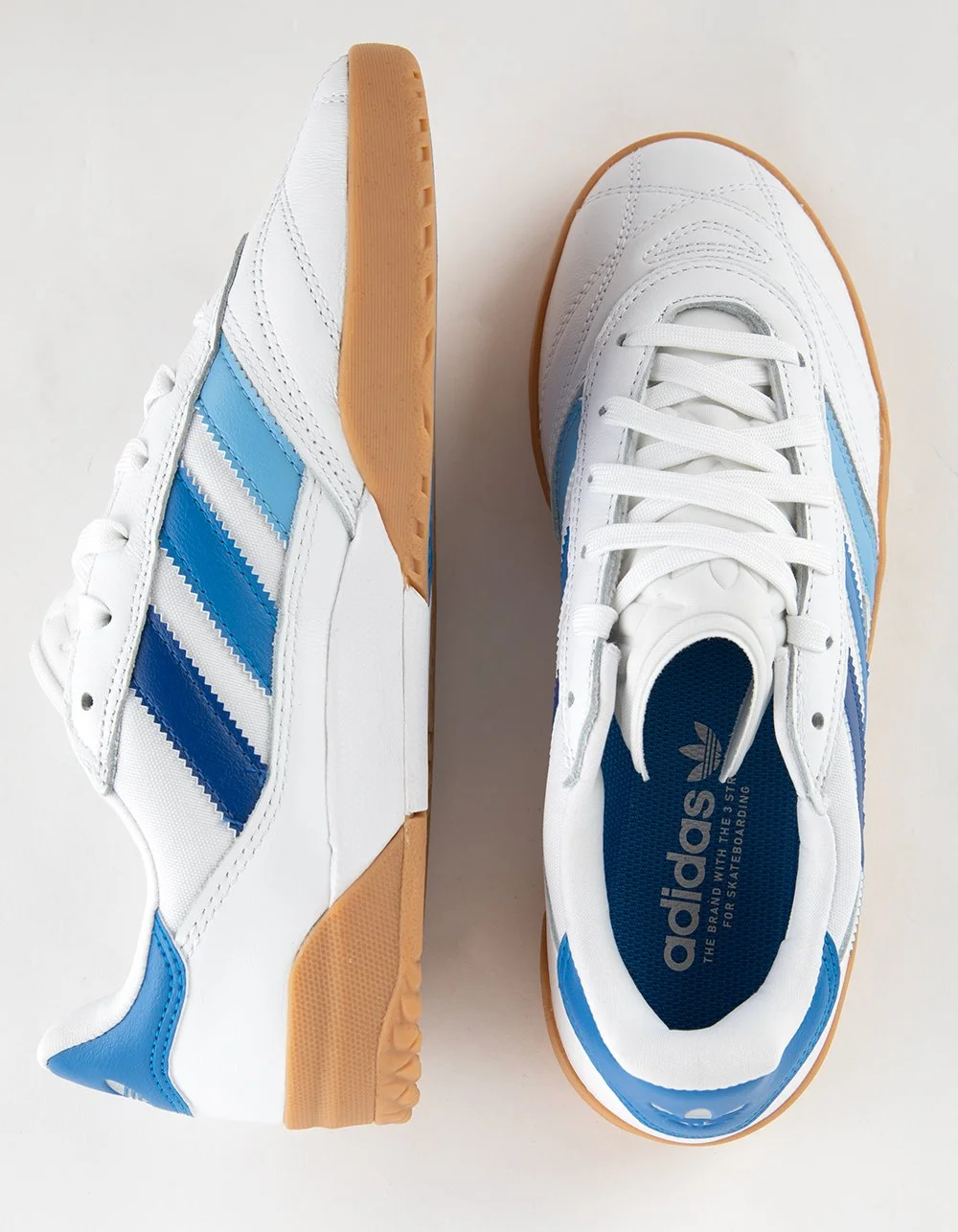 Pair of white Adidas sneakers with blue stripes and gum soles placed on a white surface.