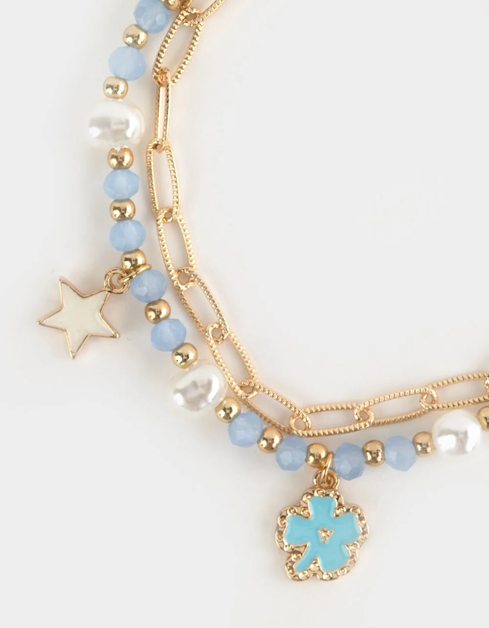 Close-up of layered gold necklaces with blue beads, white pearls, star and flower charms on white background.