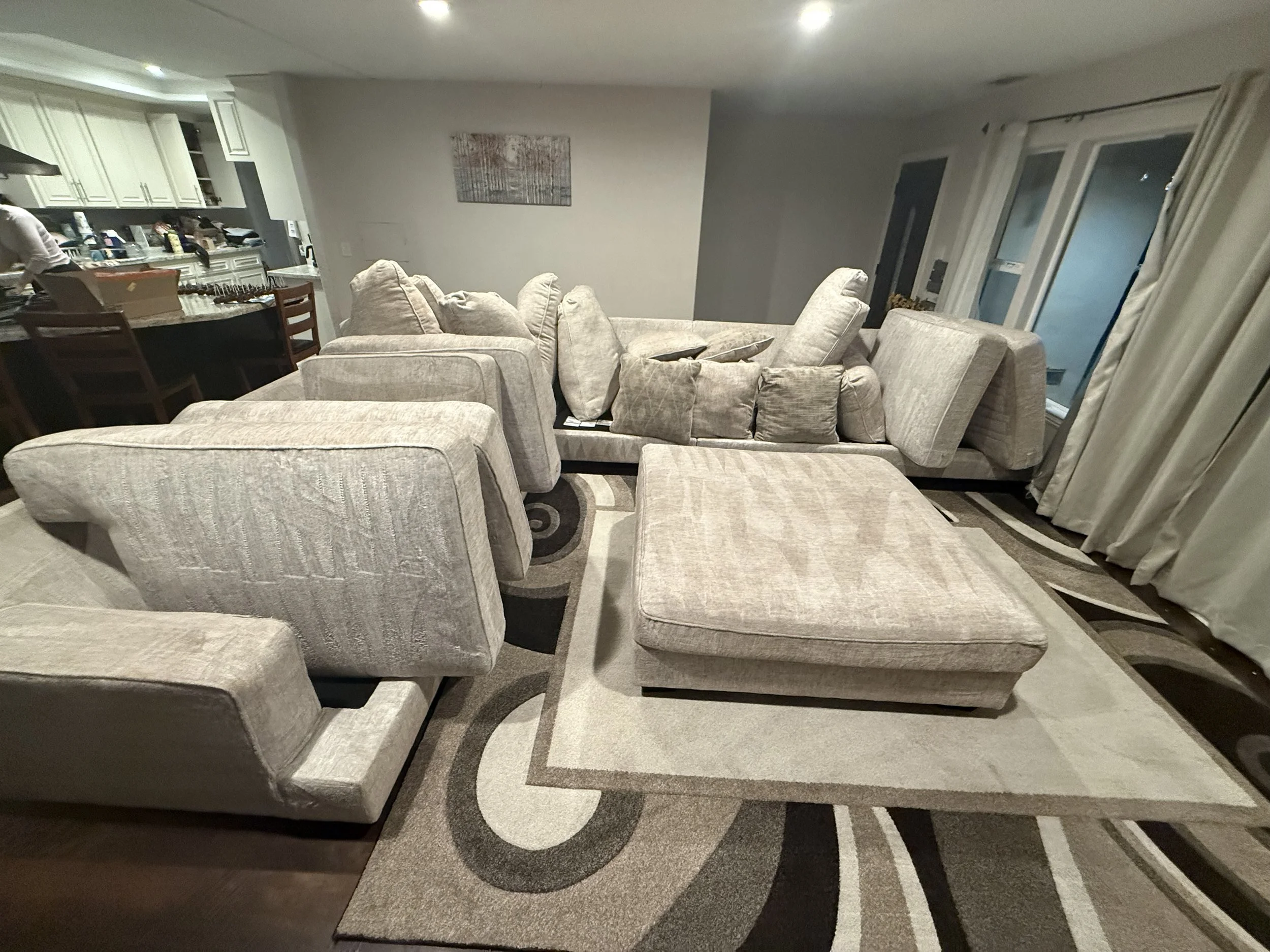 Living room with beige sectional sofa and chaise lounge, patterned area rug, and sliding glass doors with curtains.