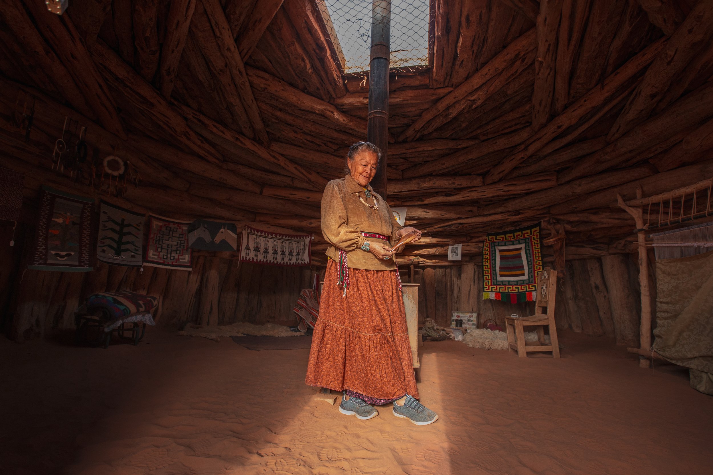  Effie Yazzie holds a weaving comb her family made for her inside her hogan. The hogan’s main source of light comes from the doorway and the hole in the roof for the furnace.  