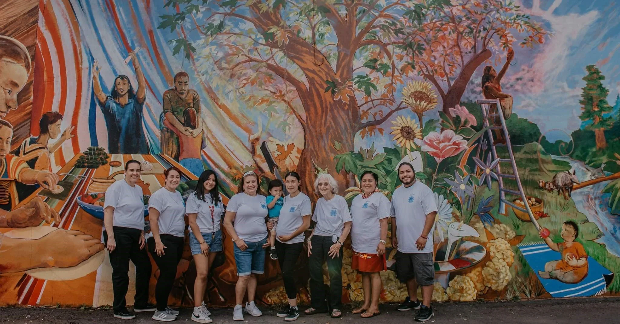 A group of people stand in front of a colorful mural