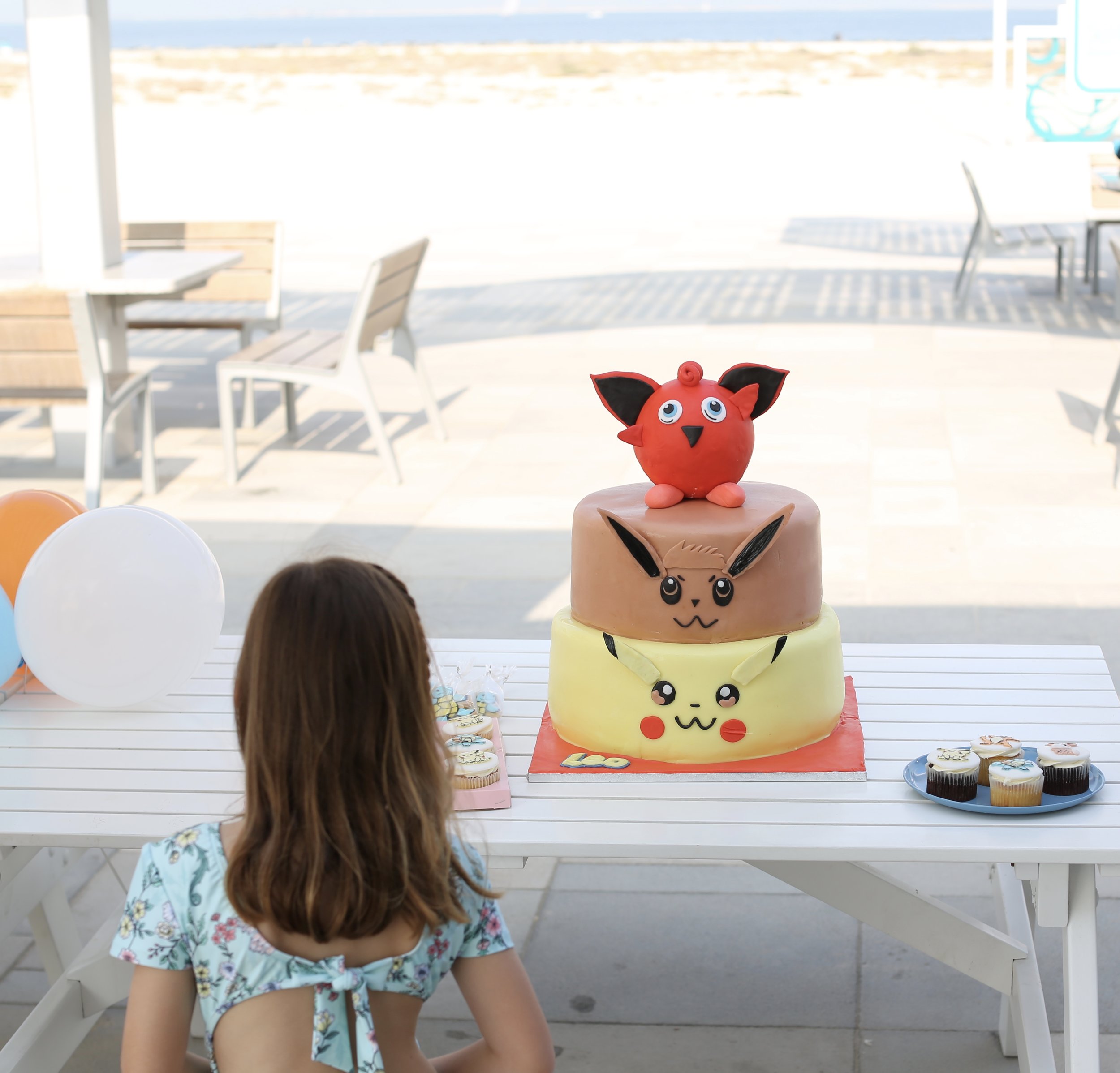 Just a girl standing in front of her three-tier Pokémon cake