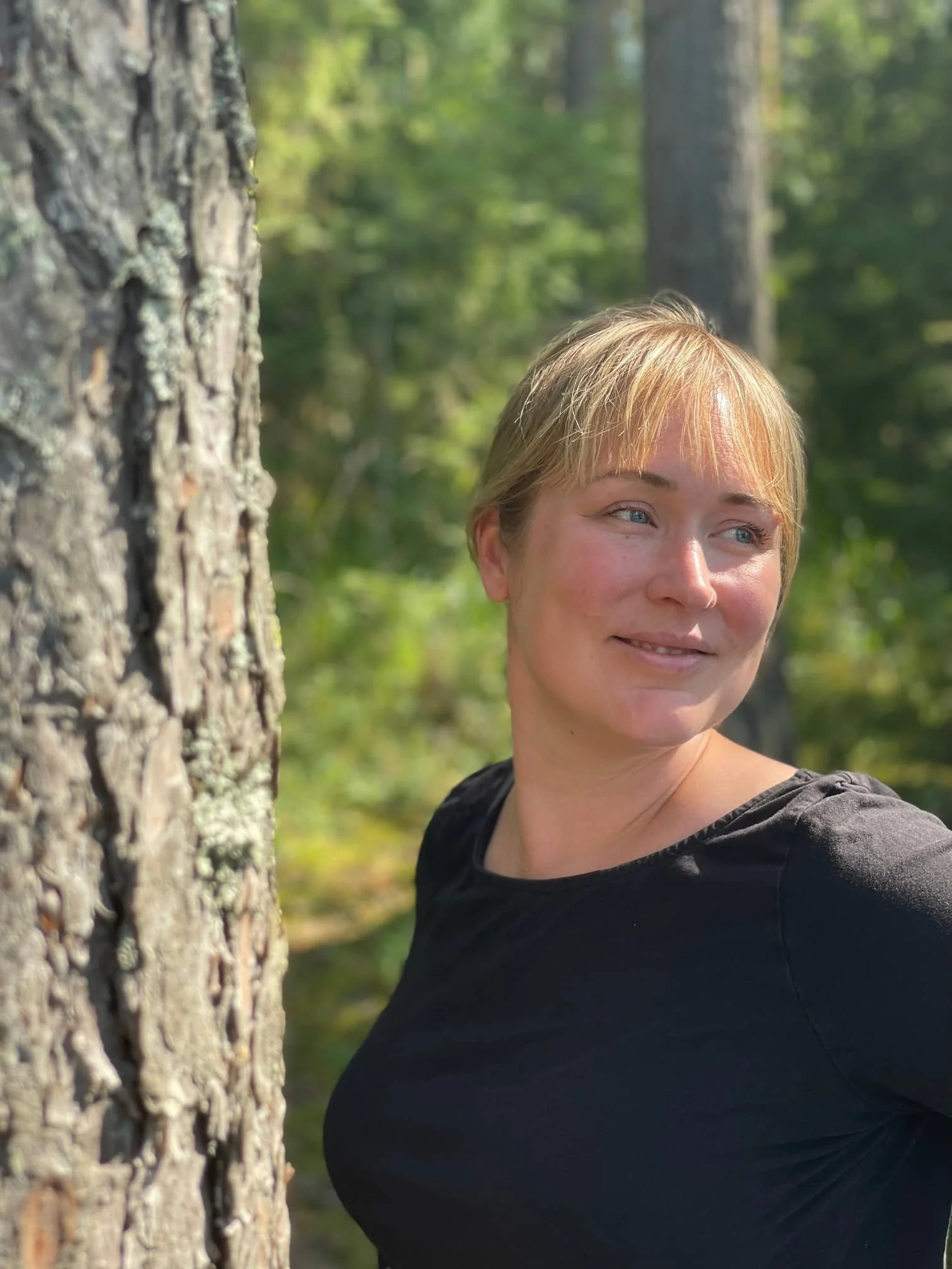 Elisa, mindfulness teacher gazing to the right smiling, in the sunlight, a forest in the background