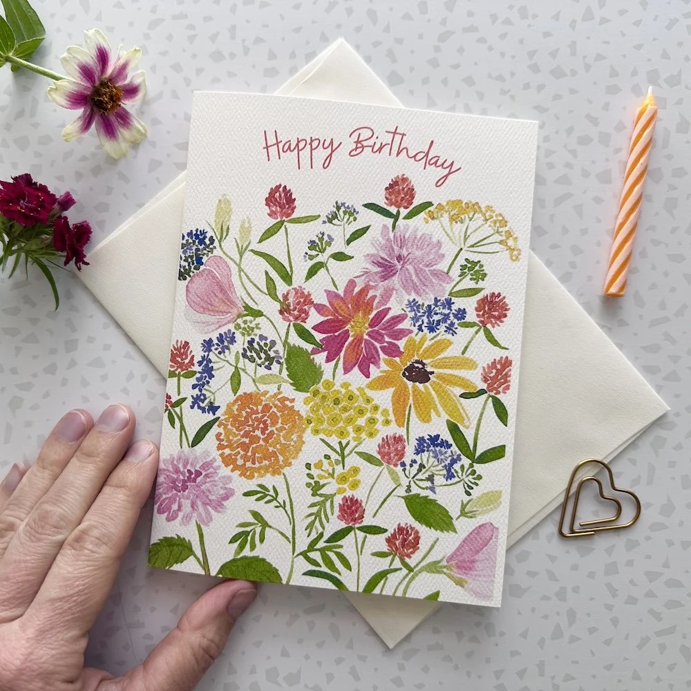 A floral birthday card with various colorful flowers and the words 'Happy Birthday' on a white textured background.