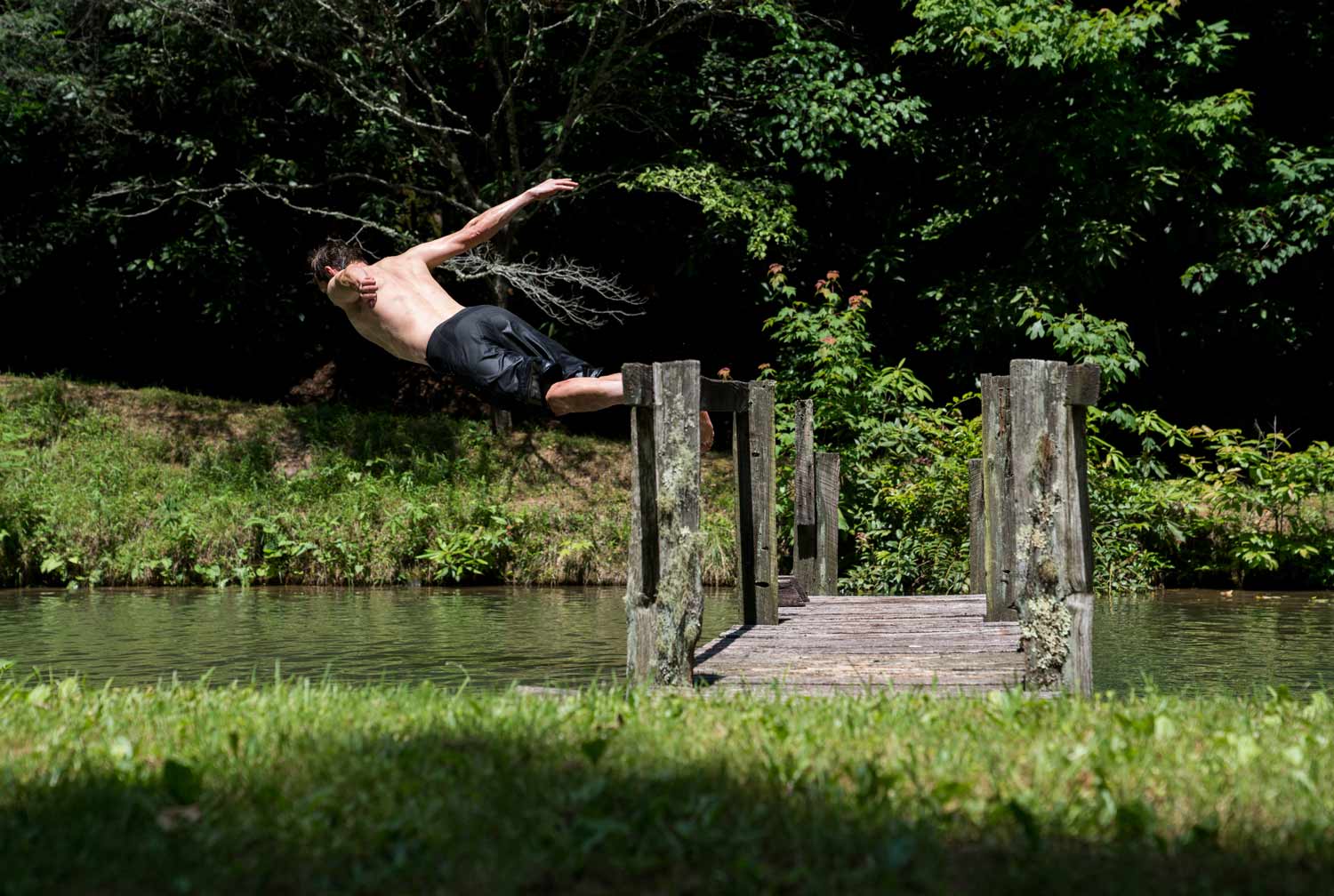 Man diving off a wooden bridge into the water at the Bike Farm