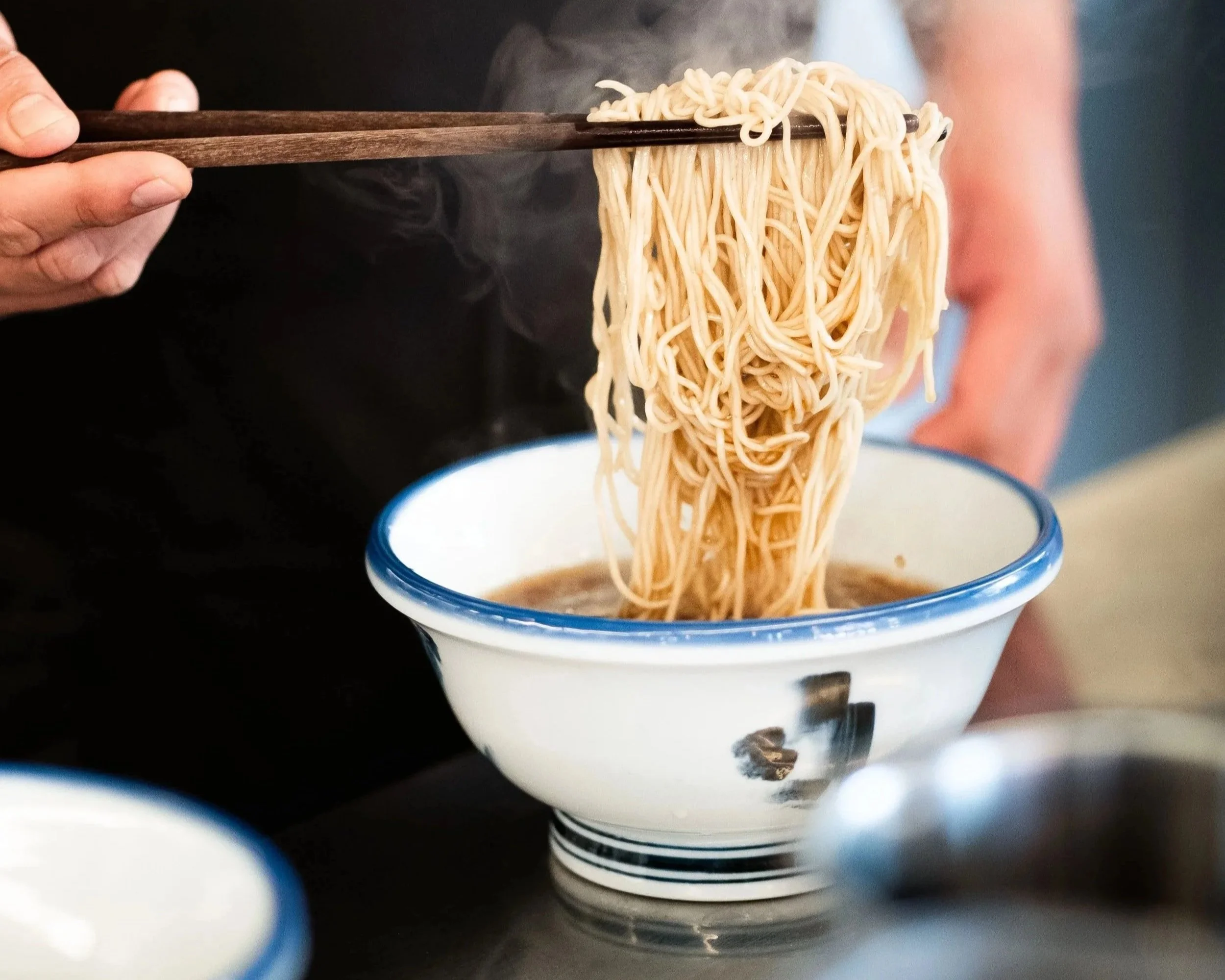 Fresh noodles being folded into a hot bowl of ramen.
