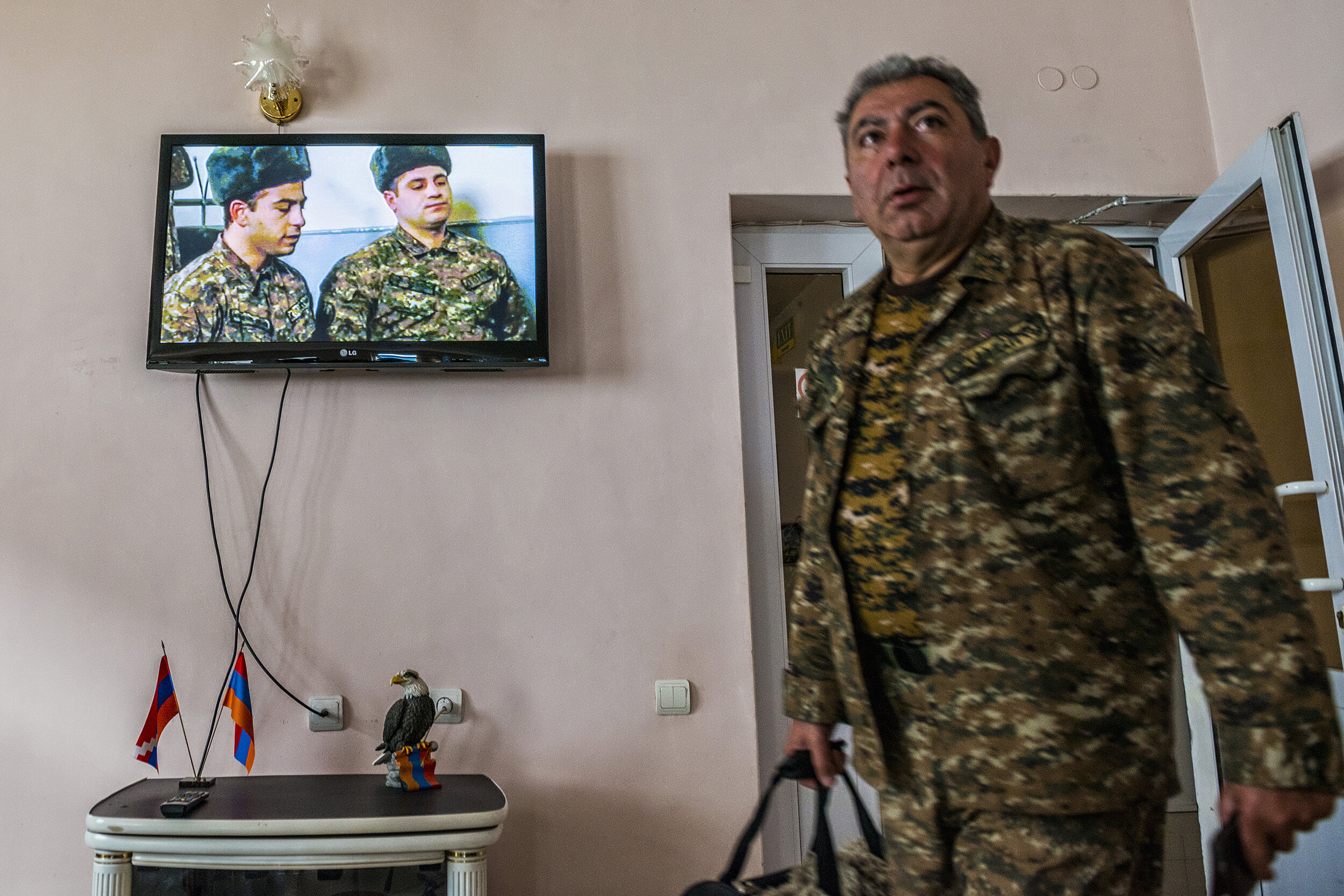  An NKR soldier exits the Nairi Hotel in Stepanakert, Nagorno-Karabakh while a TV plays a military film above the flags of Armenia and the NKR, their denizens inextricably linked. 