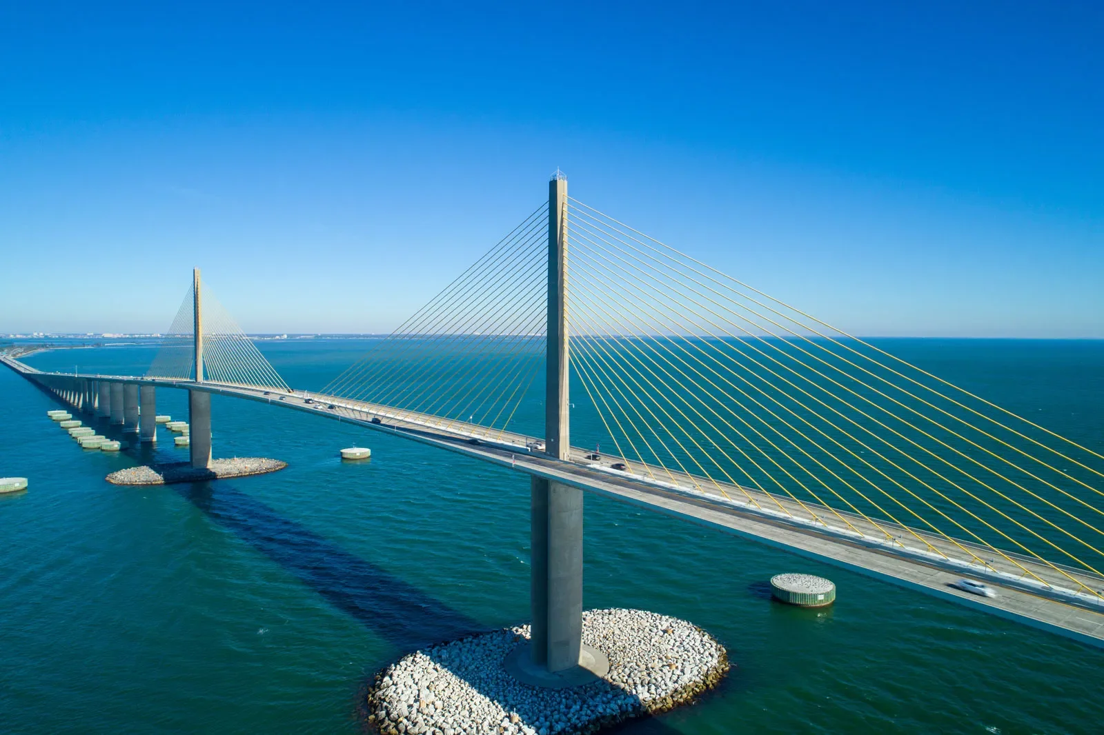 A modern cable-stayed bridge with tall pylons and yellow cables over the ocean on a clear, sunny day.