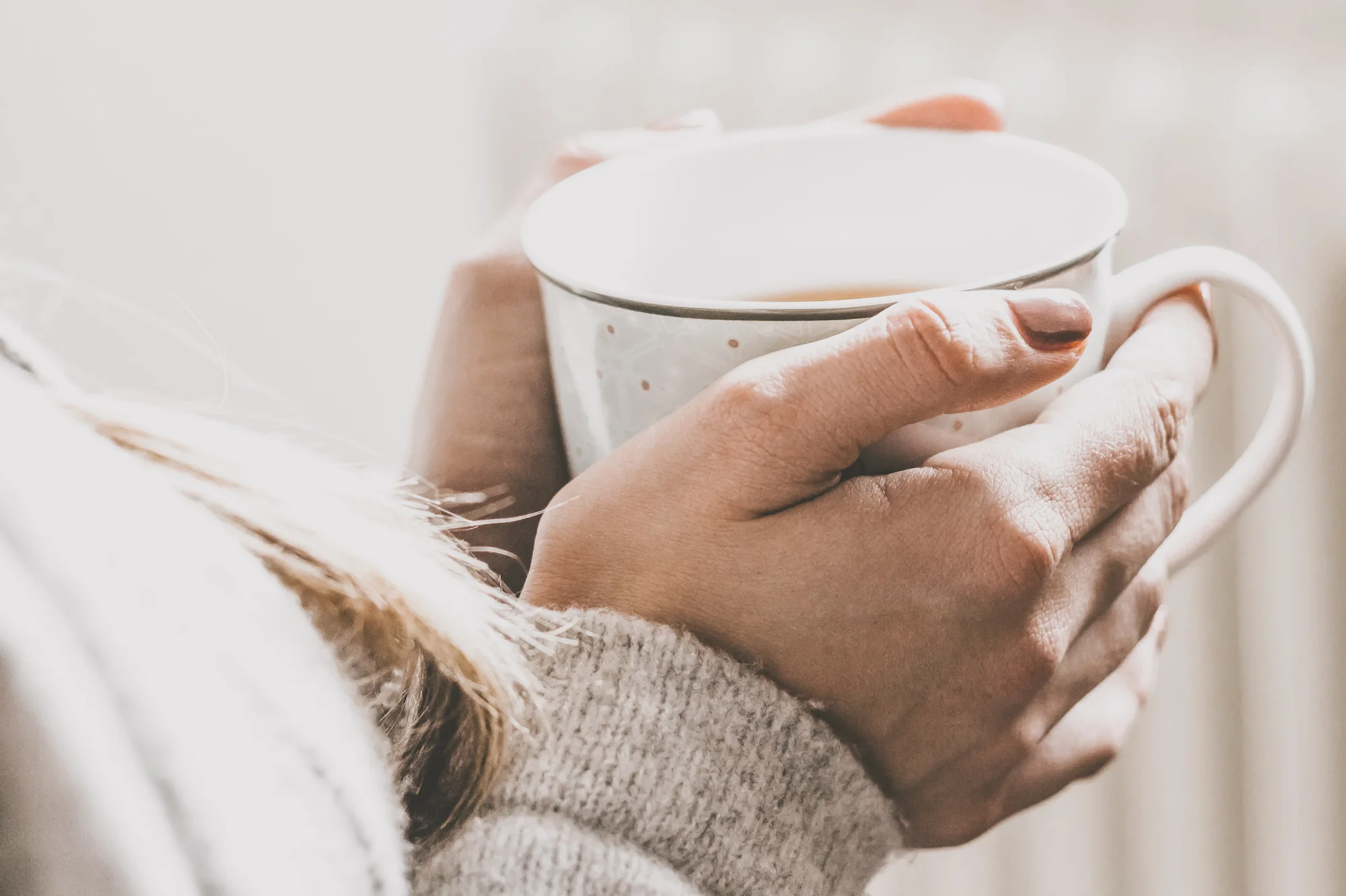 Junge Frau wärmt Hände an Teetasse