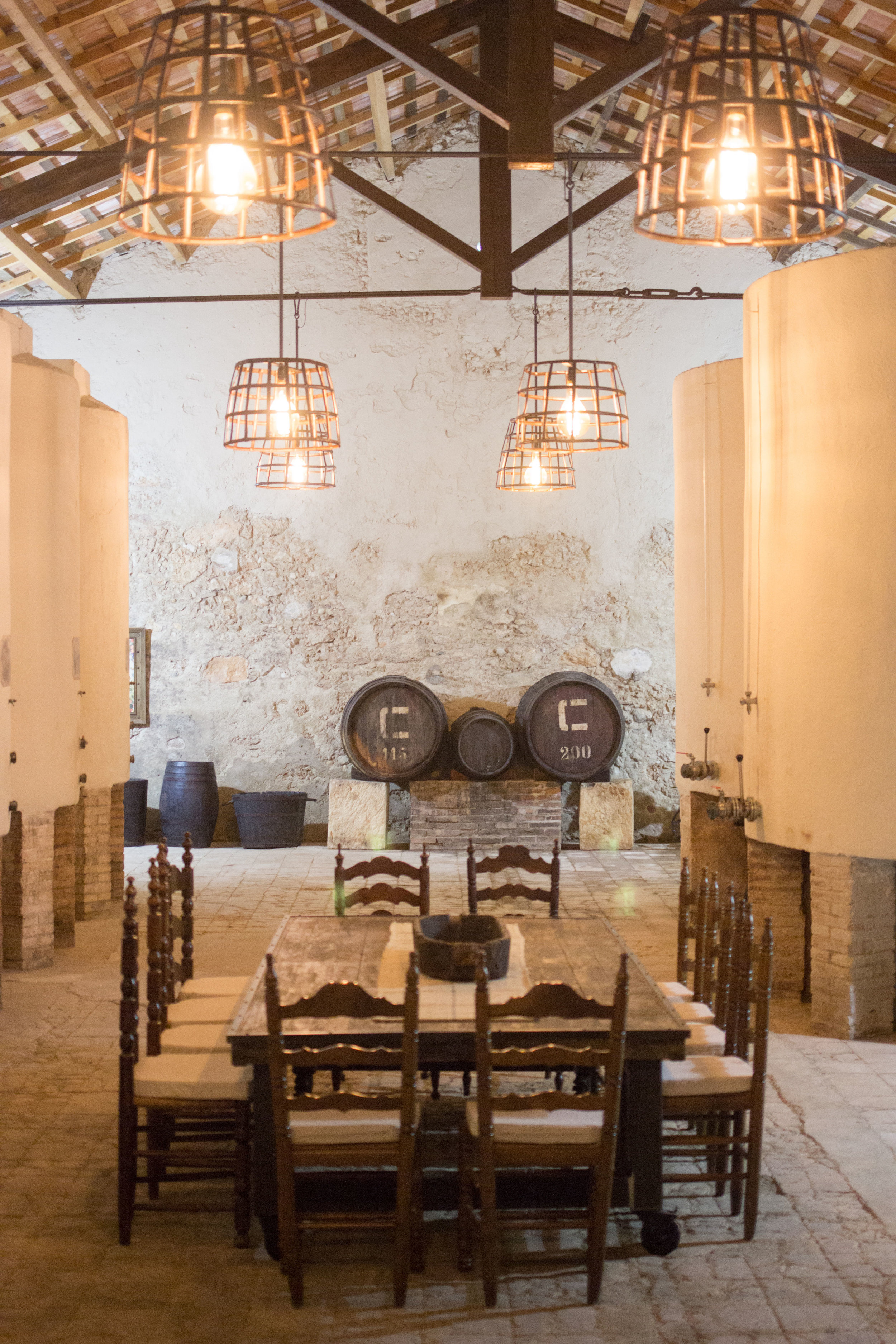 Design light fixtures, high ceiling, large cool space with a handmade upcycled table in the middle and vintage wine barrels in the background