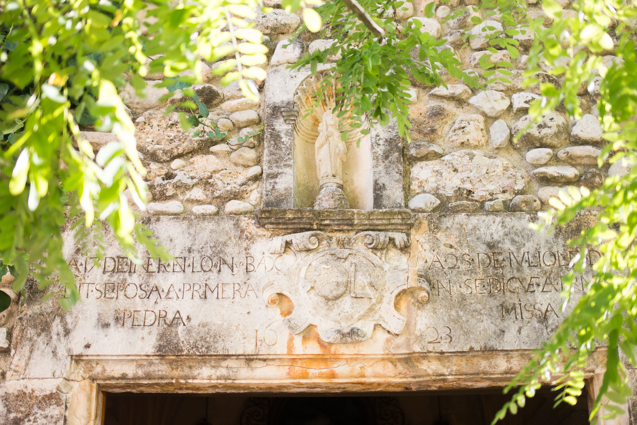 Historical sign of the chapel with latin inscription and the heraldry symbol of Mas Palou, as well as a small figure of Mary