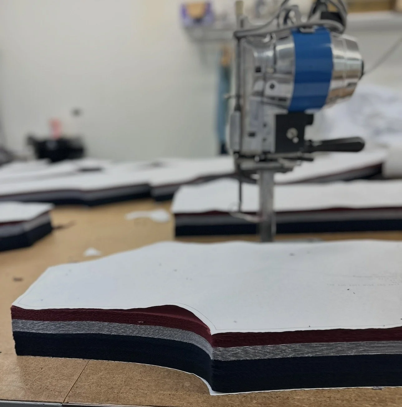 A piece of layered fabric or paper in white, red, gray, and black colors on a wooden surface with a cutting machine in the background.