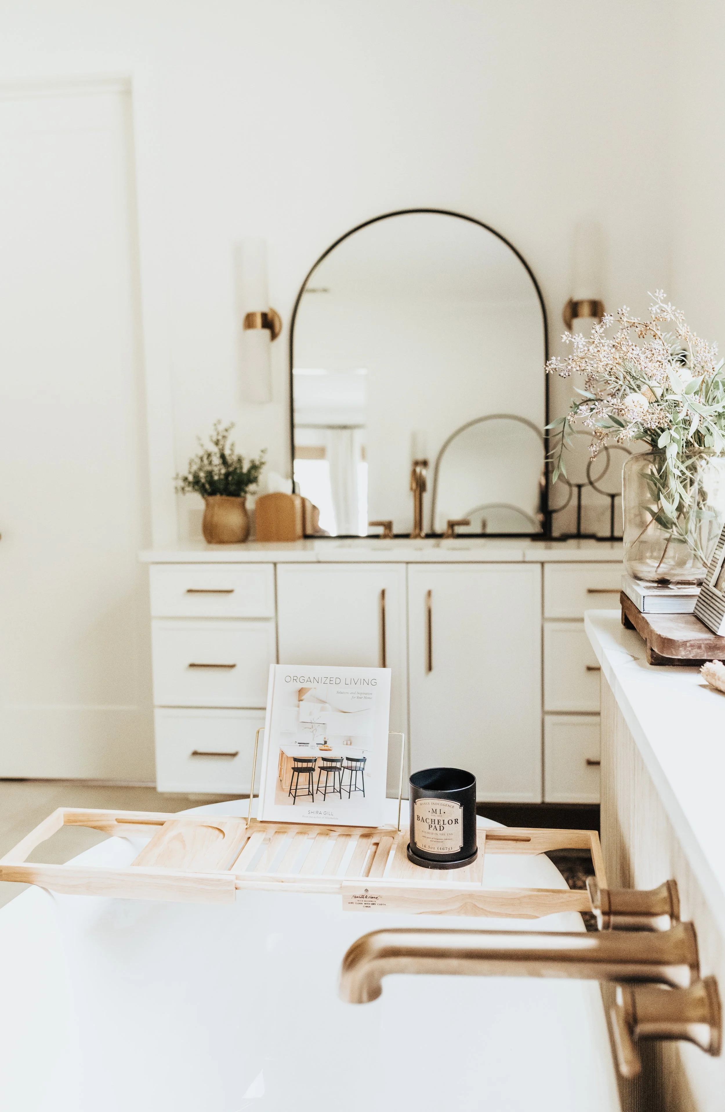close up shot of soaking tub with book, candle, and gold faucet and flowers near a window