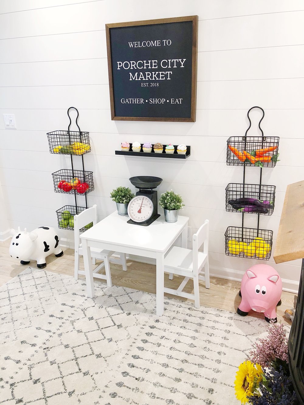 A grocery store setup in a playroom, with 2 sets of 3 wire baskets hanged on the wall.