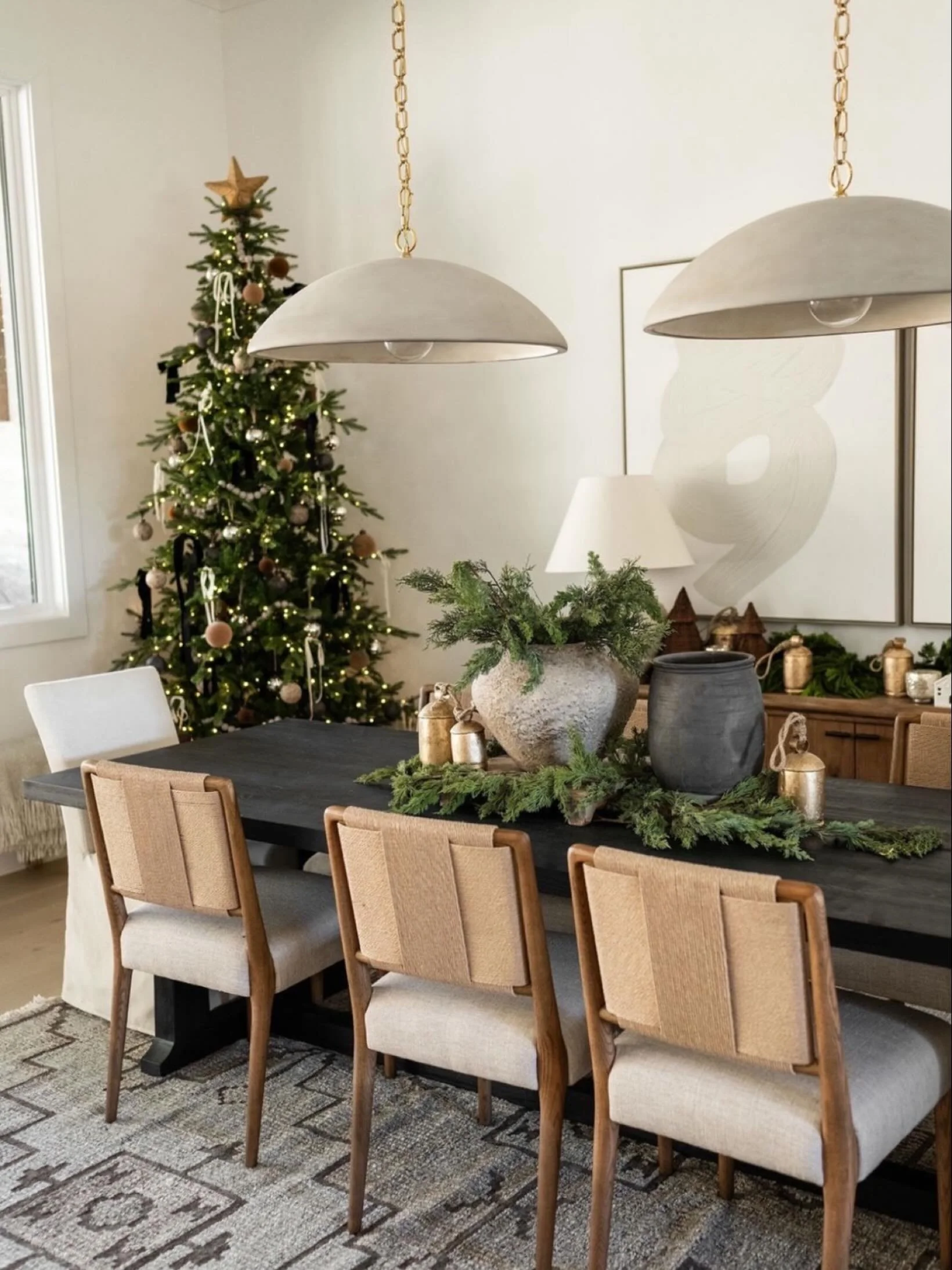 A dreamy Christmas dining room moment 🤍🎄 Layered neutral holiday decor, fresh evergreen branches, stone vases, gold bells, and a softly lit Christmas tree make this space feel warm and inviting. Perfect inspo for Christmas dining room styling, neut