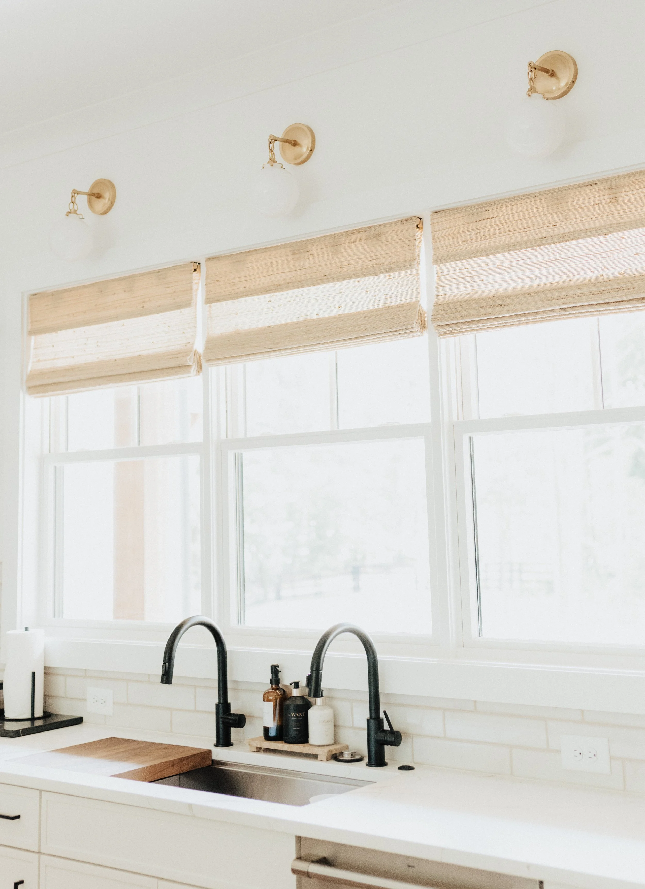 white walls with three windows and gold pendants and roman shades