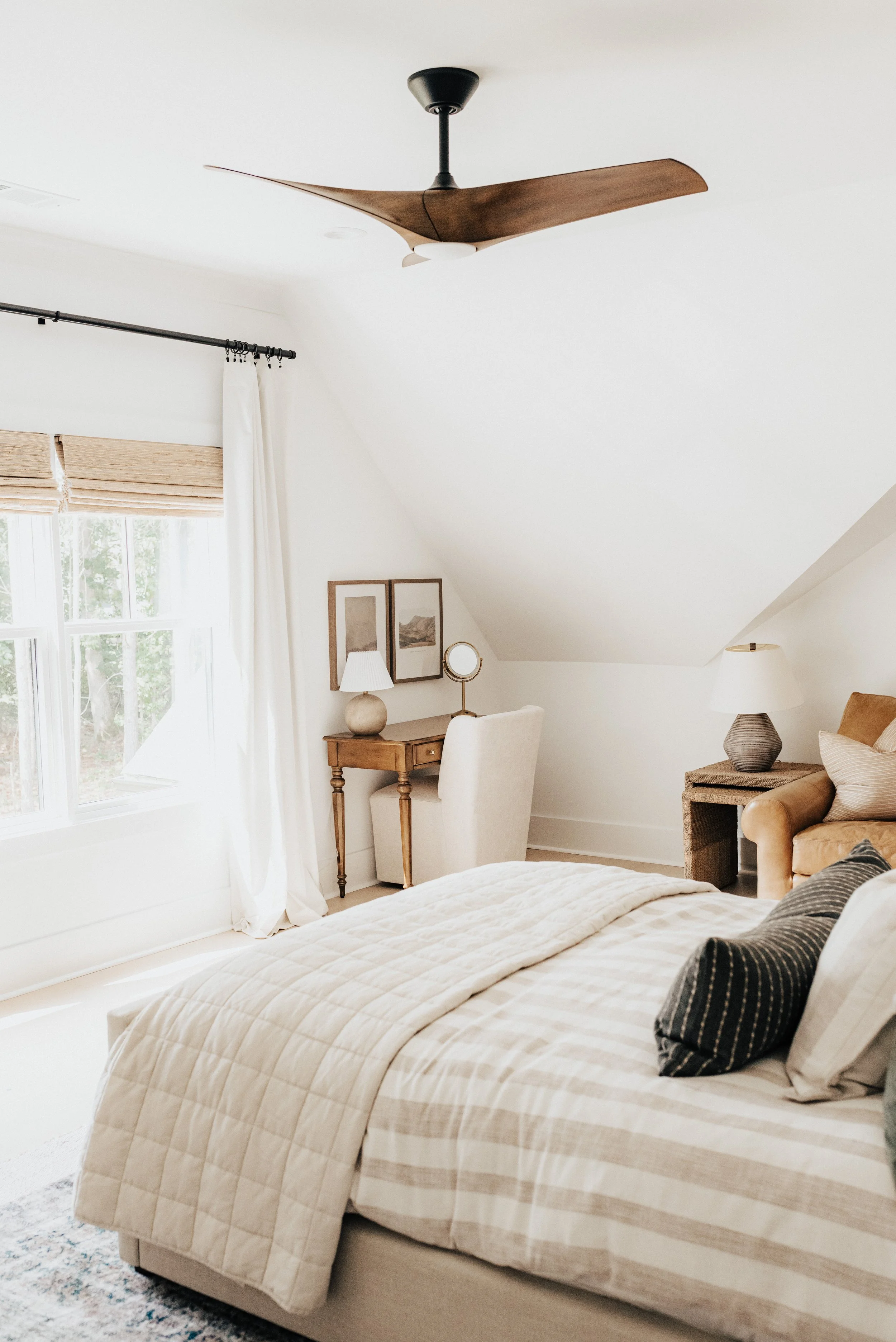 bright classic guestroom designed with white walls, a neutral bed and a wooden desk