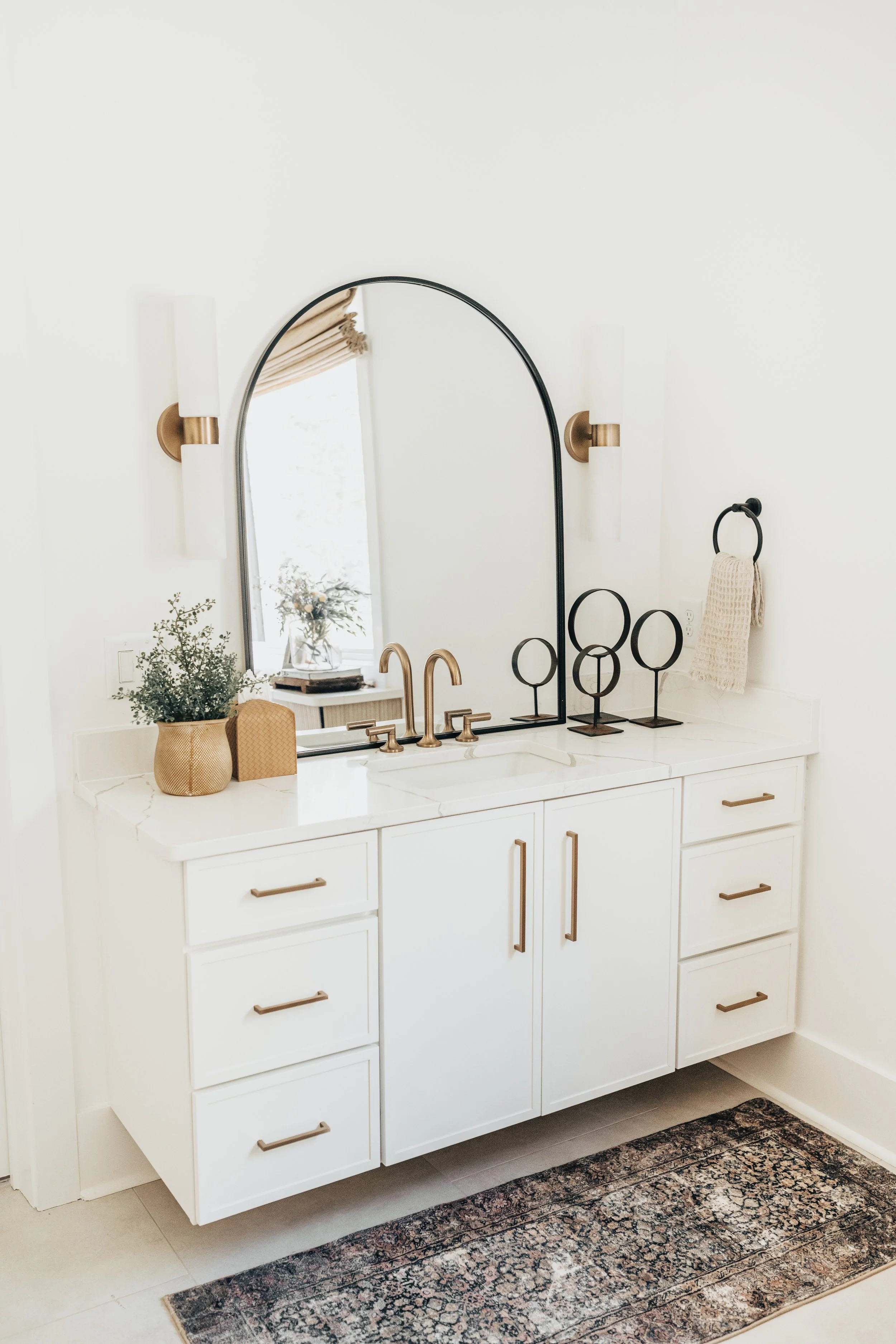bathroom sink on white cabinet with gold pulls and black matte mirror and decor