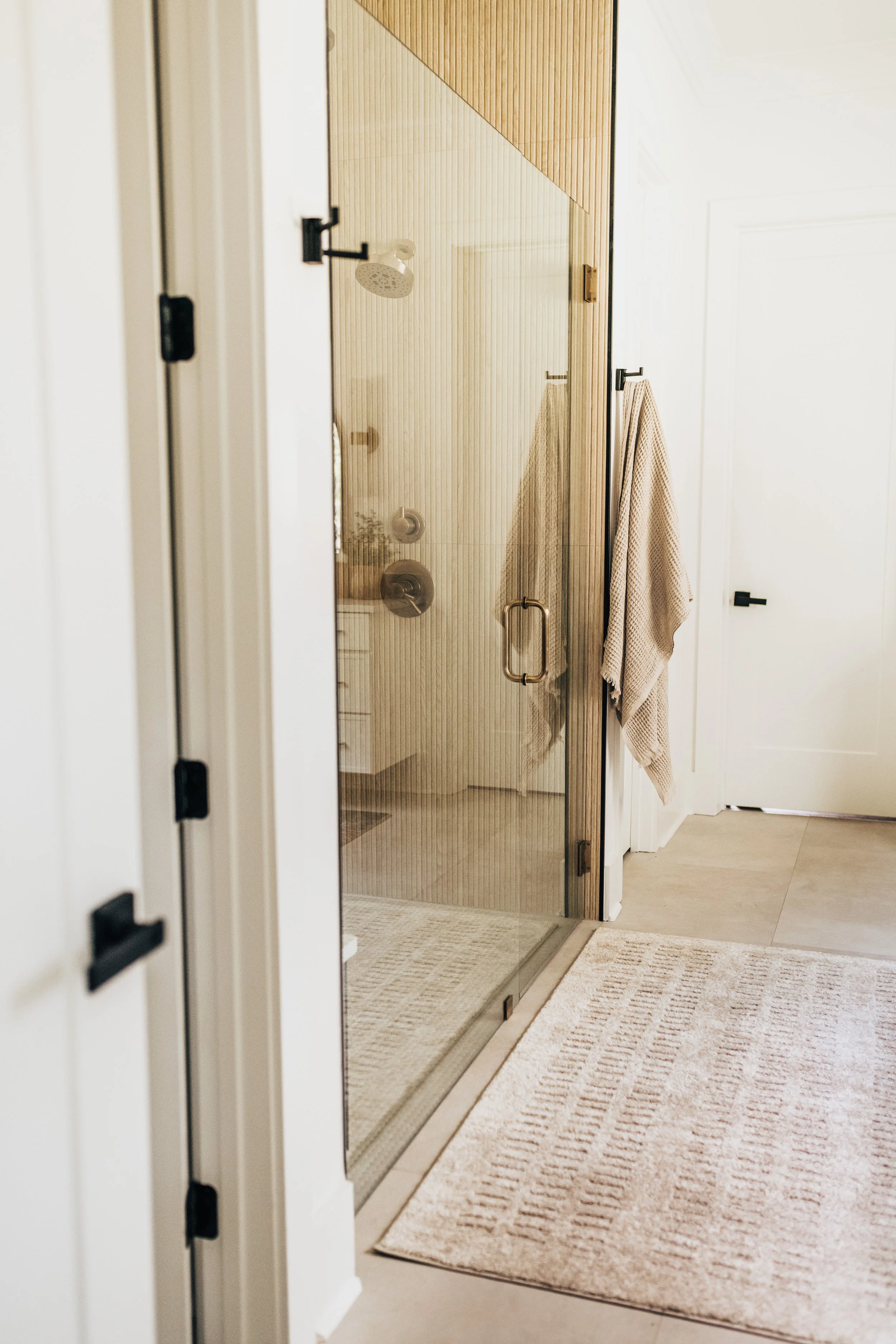 glass shower with wood tile and neutral towels and rug