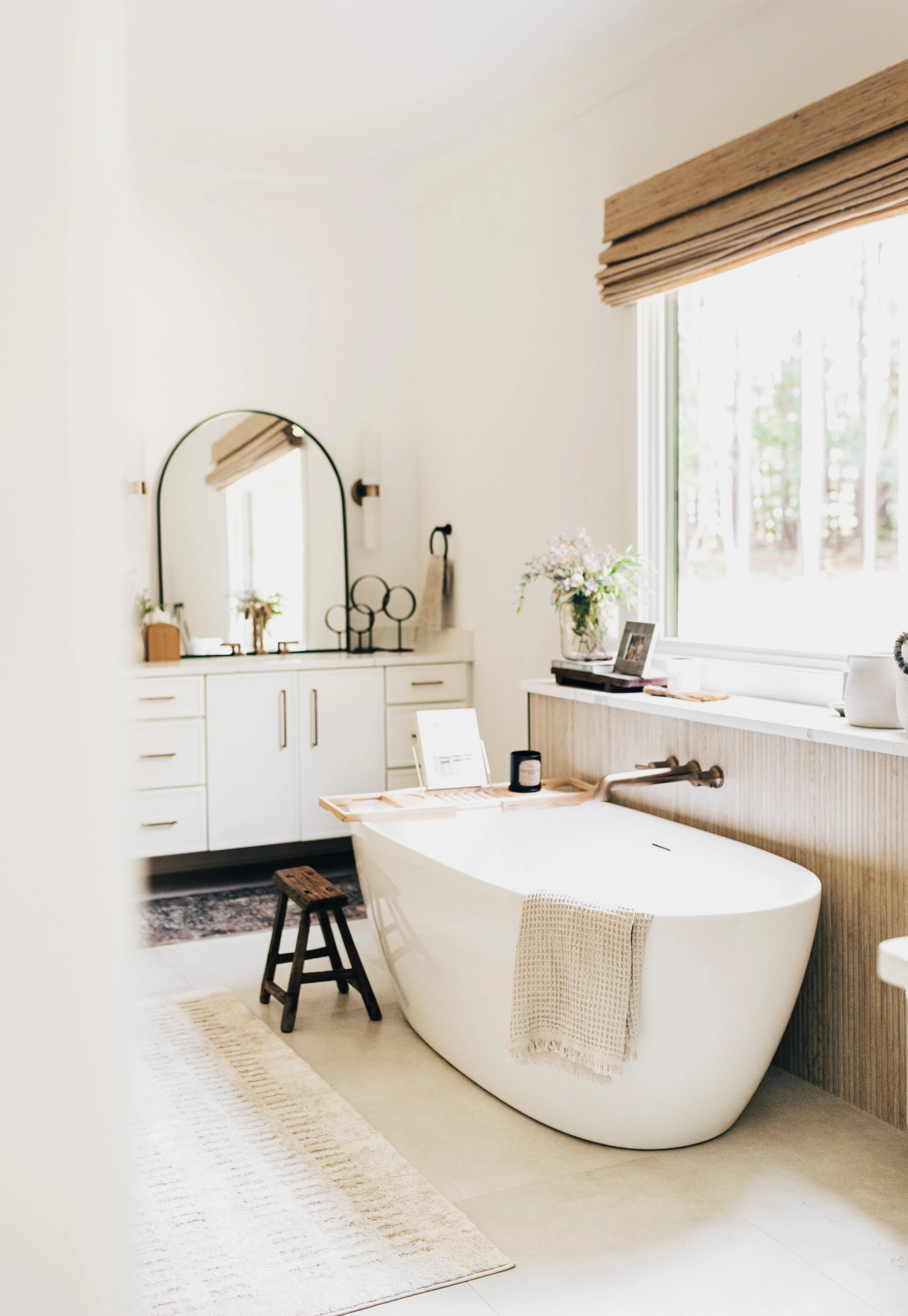 view through a door or a primary bathroom with white soaking tub and cabinet and mirror next to a large window