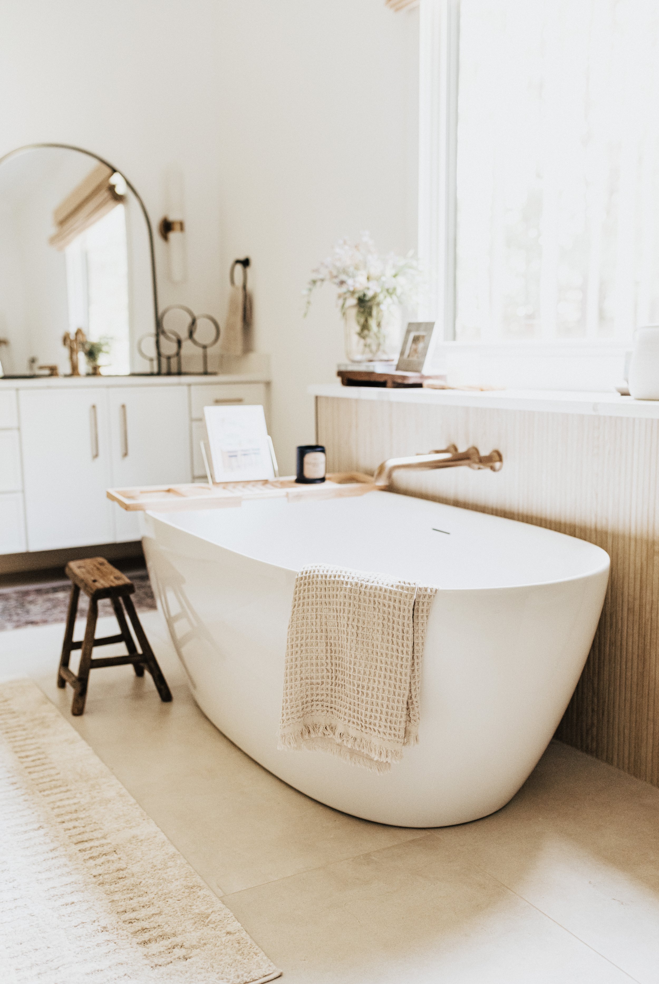 large white bathroom soaking tub with gold fixtures and white cabinet with black mirror