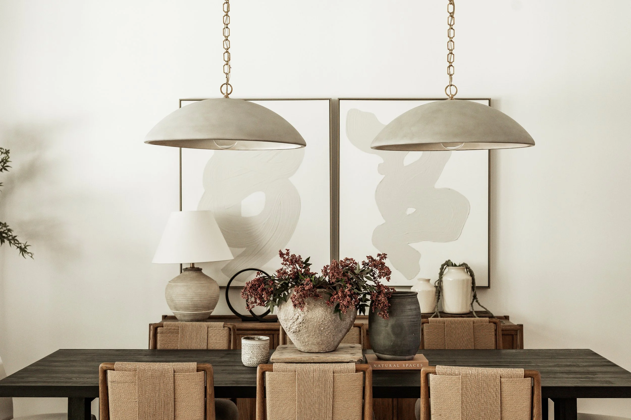 modern dining room table with large cement pendants overhang with faux florals and large white pictures