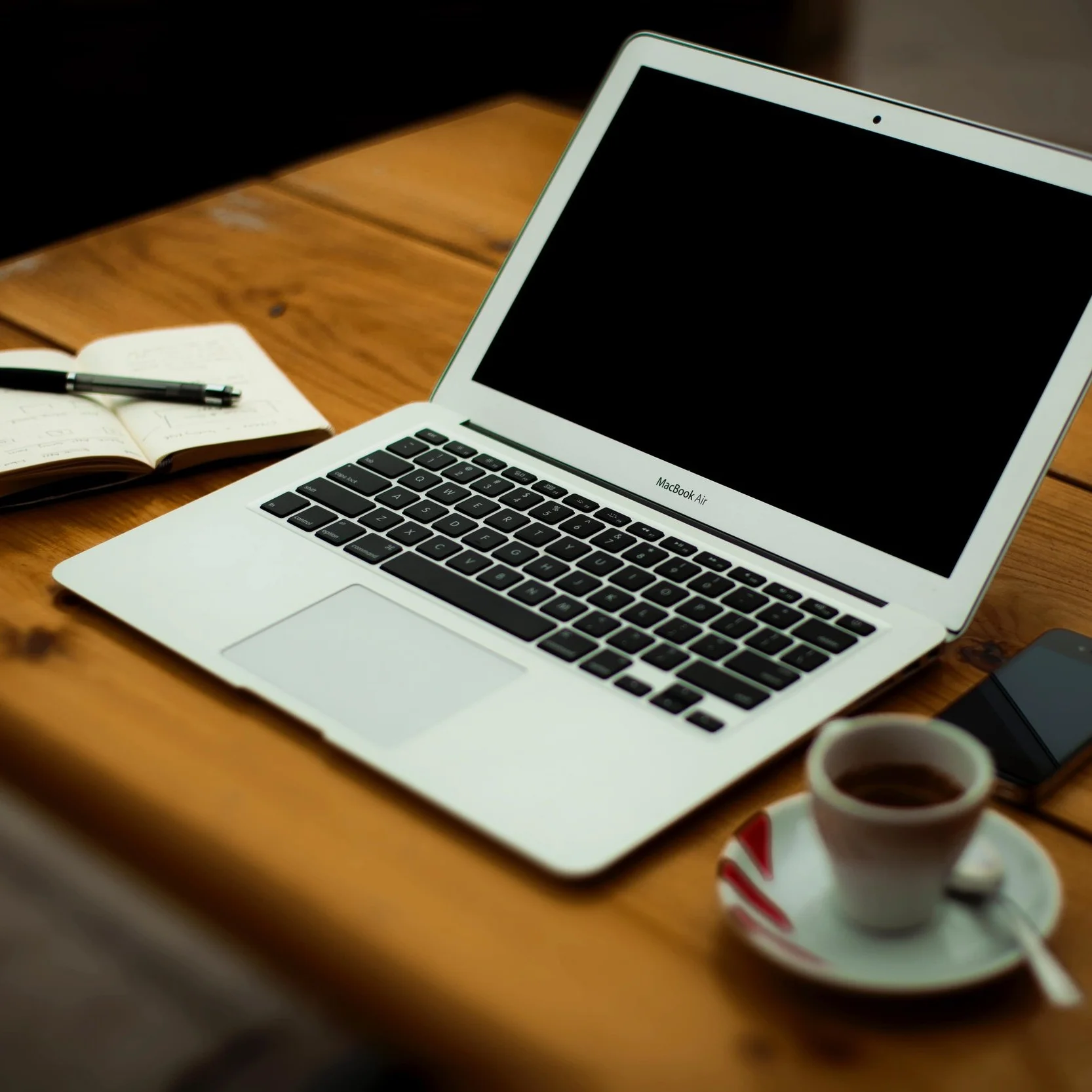 MacBook laptop with black screen and a notebook beside it.
