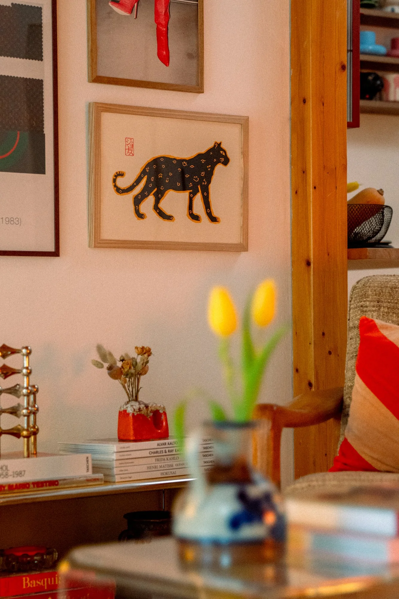 Room with wall art of a stylized black panther, decorative items, and a small vase with yellow tulips in the foreground.