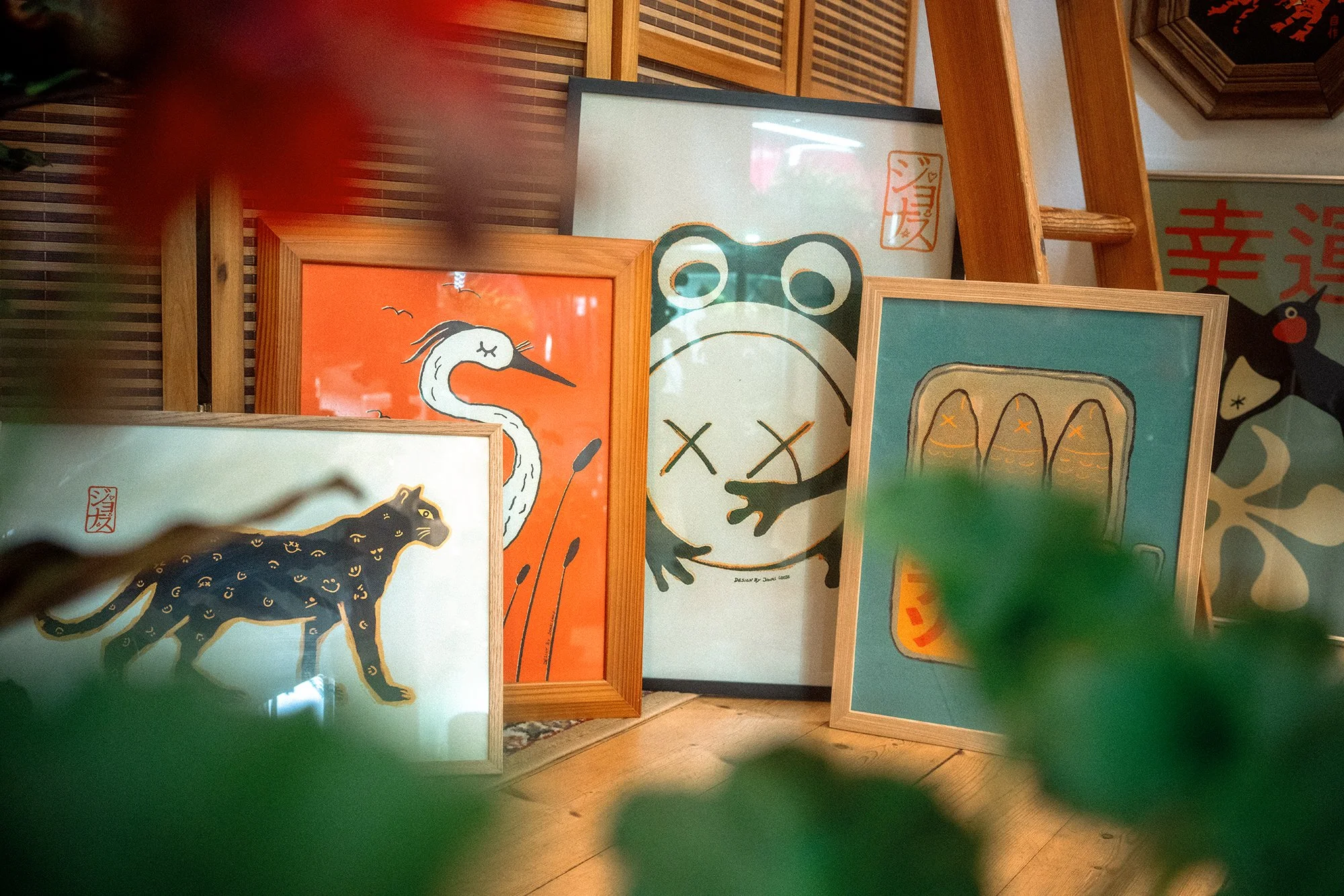 Collection of framed art prints featuring various animals, including a black panther, a white heron, a frog, and a fish, displayed on a wooden surface with some greenery in the foreground.