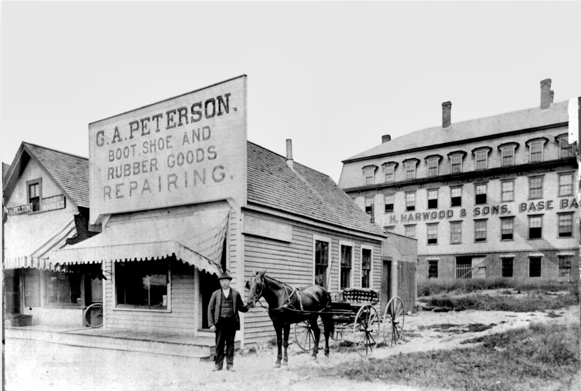 G.A. Peterson&rsquo;s boot, shoe, and rubber repair shop in the foreground, with the landmark H. Harwood &amp; Sons baseball factory in the background. Shoe work and baseball manufacturing were both important parts of Natick&rsquo;s story. 

Image fr