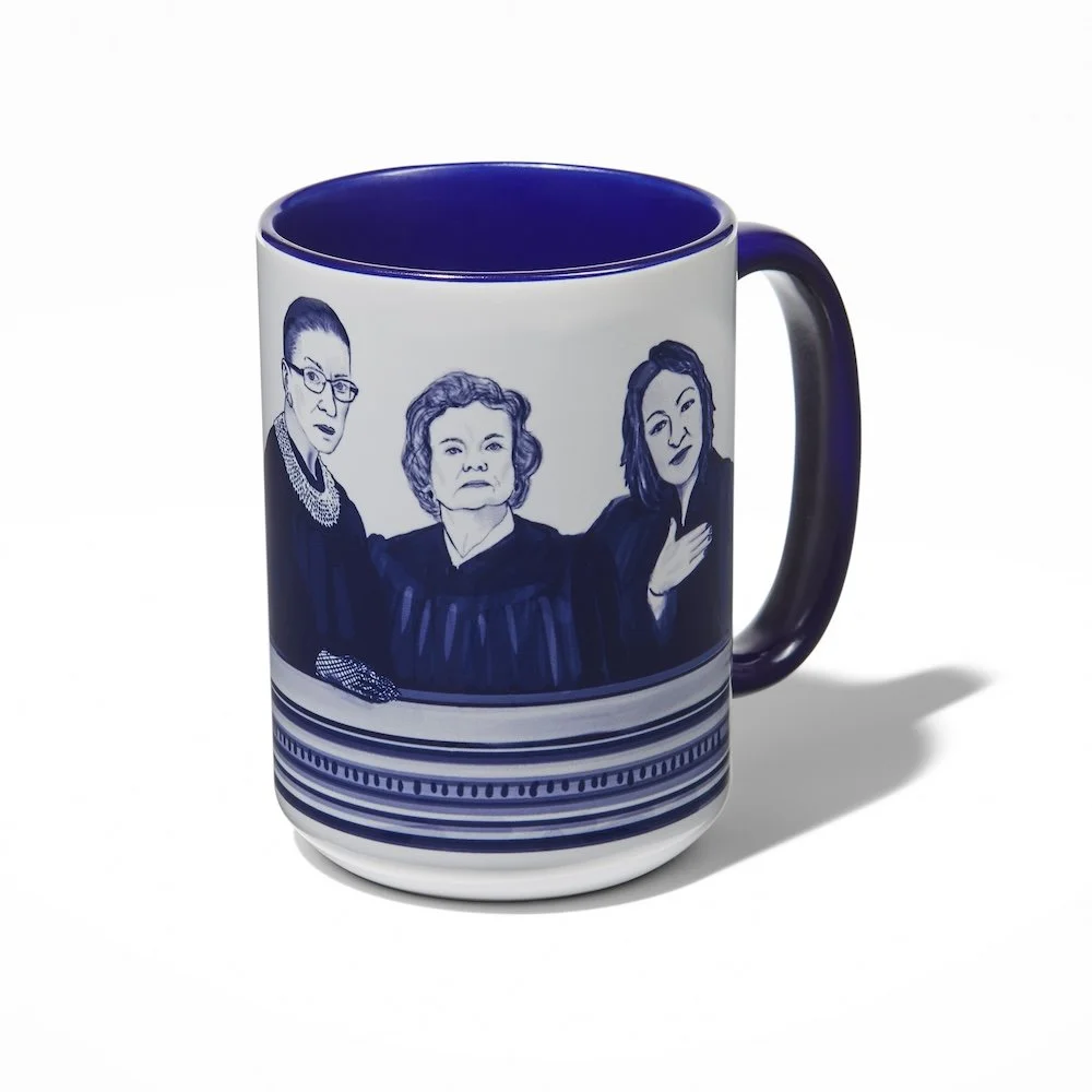 A white mug with a blue interior and handle featuring illustrations of three women in black robes, with a layered striped design around the base.