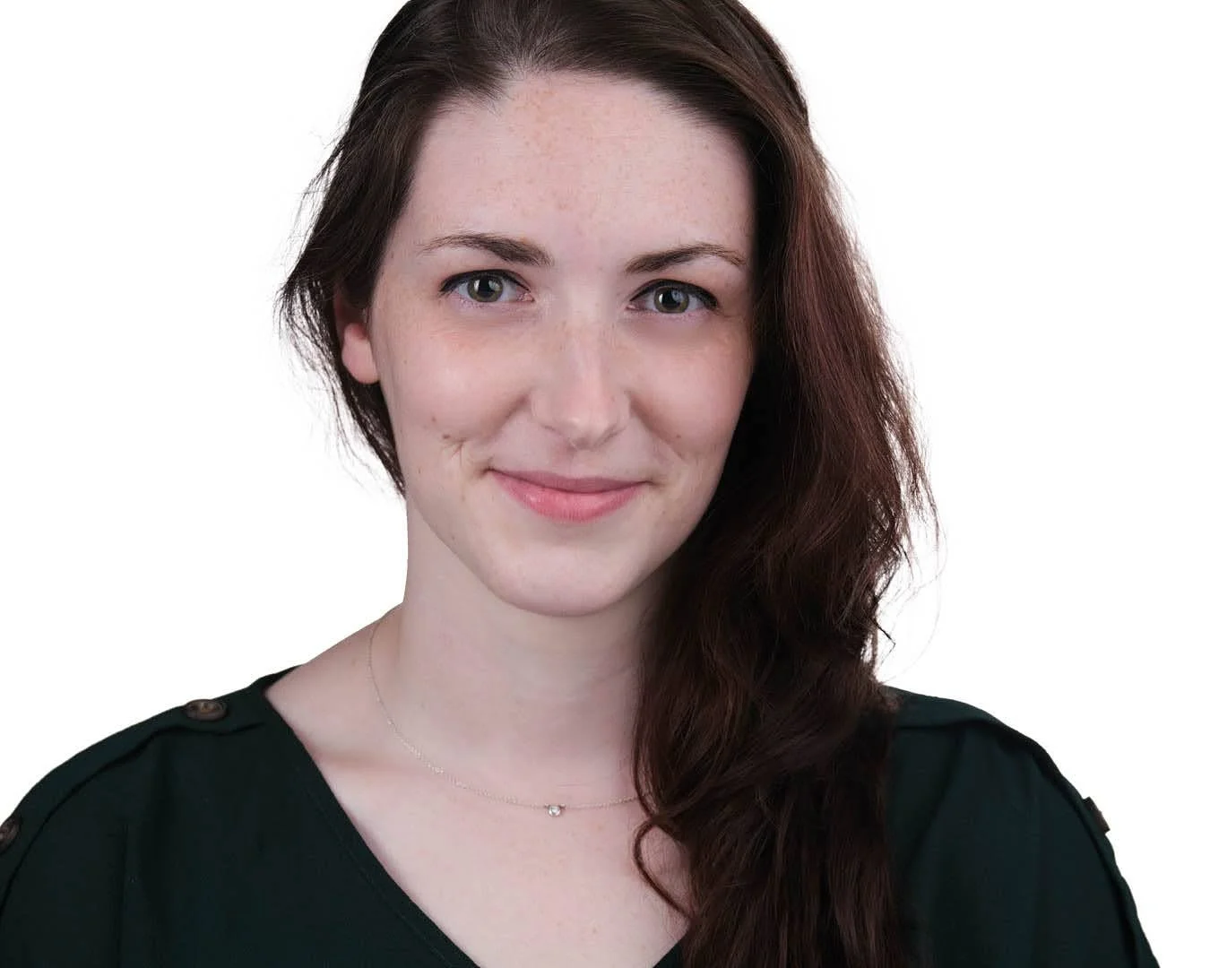 A woman with long brown hair, fair skin, and green eyes is smiling and looking at the camera. She is wearing a black top with button details on the shoulders and a delicate necklace, against a white background.