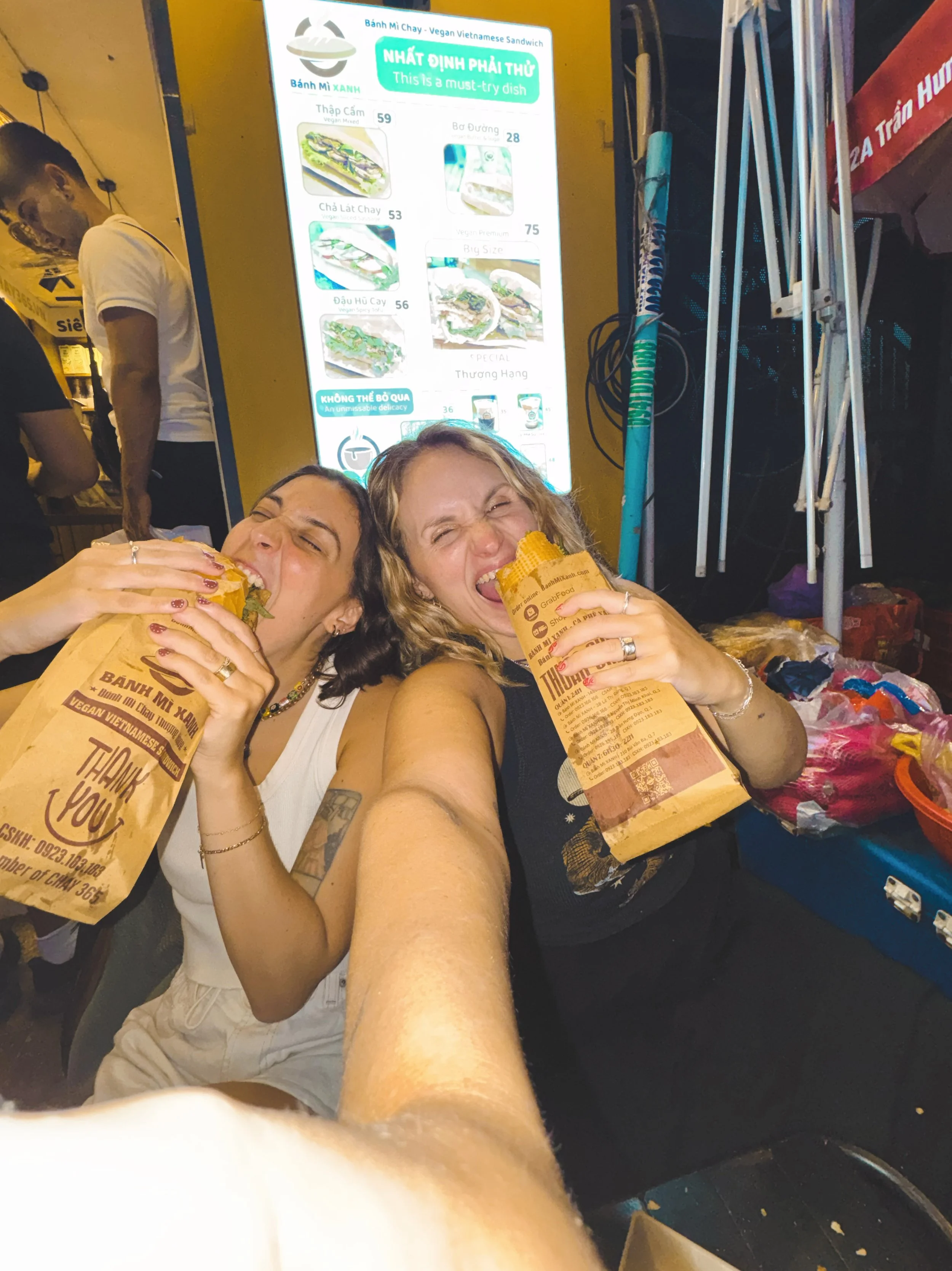 two girls eating bahn mi on the street in vietnam