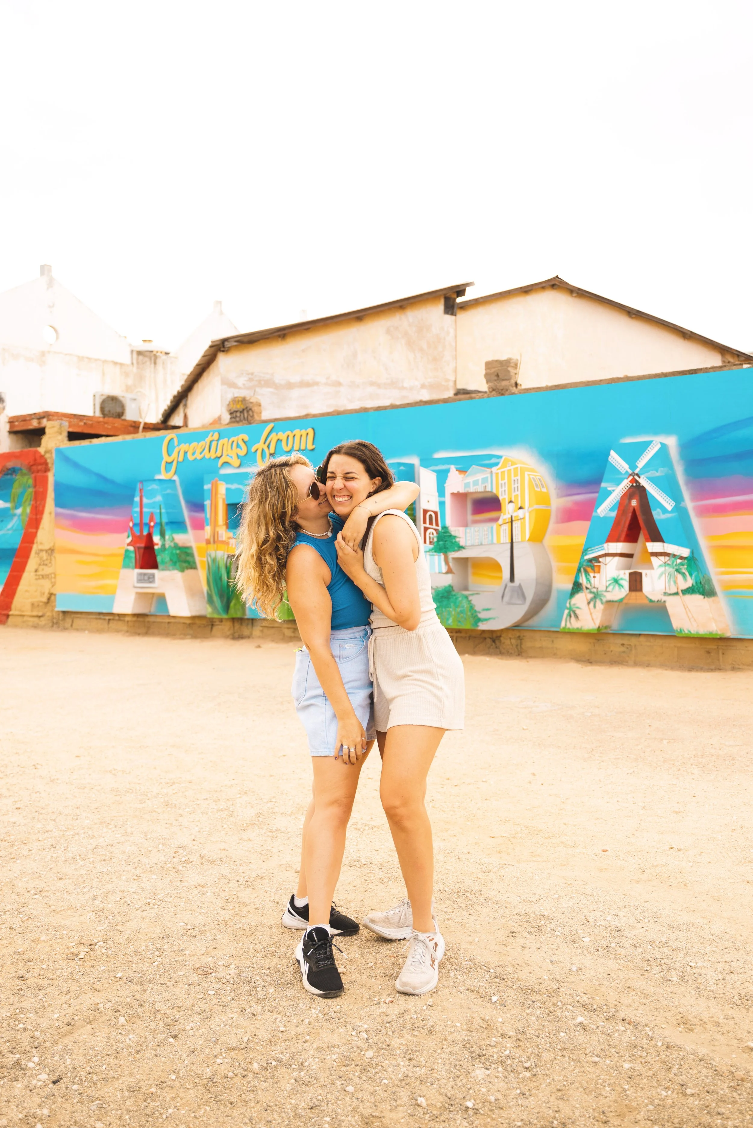 two girls hugging in front of greetings from aruba sign