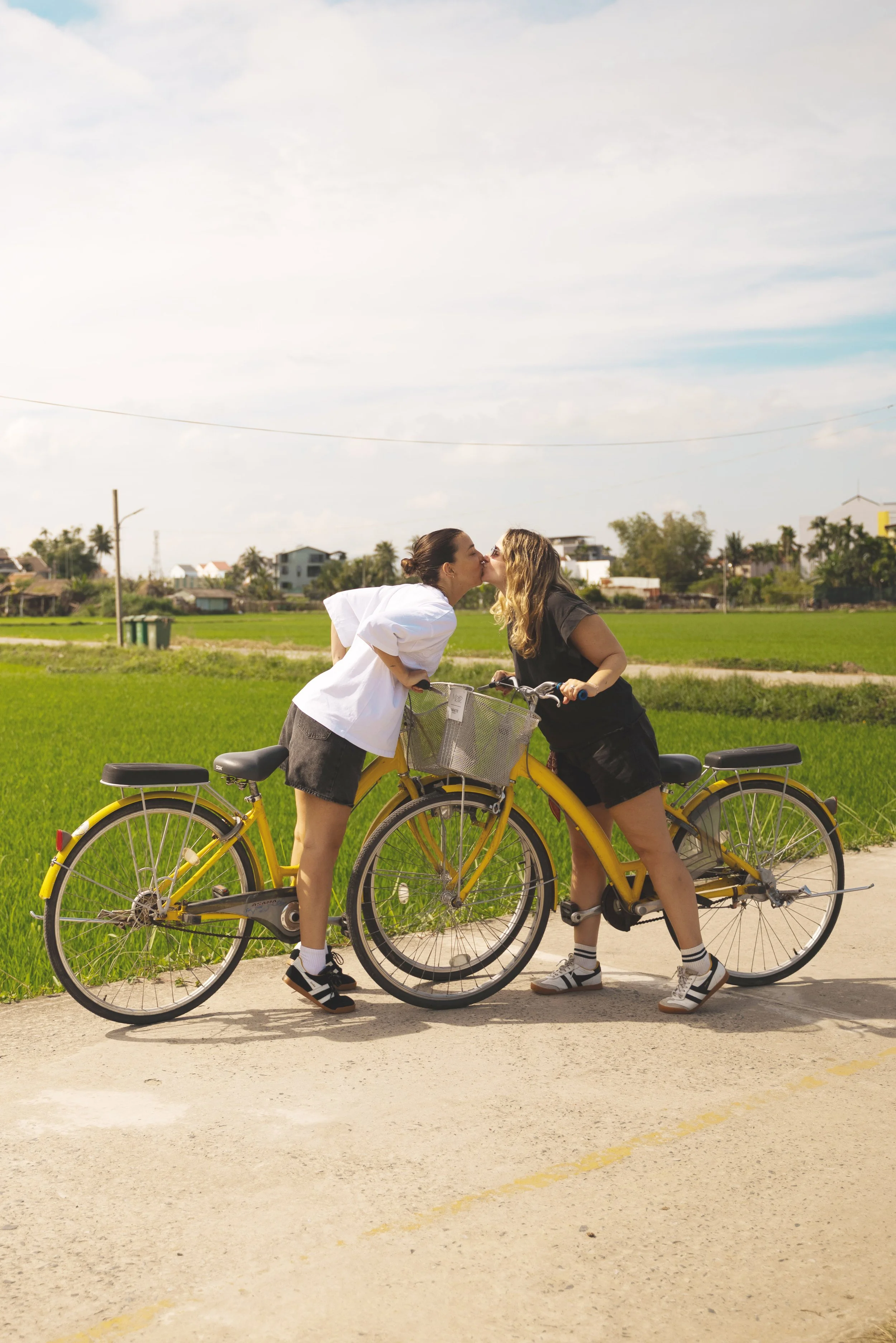 two girls kissing on bikes at rice paddy fields hoi an