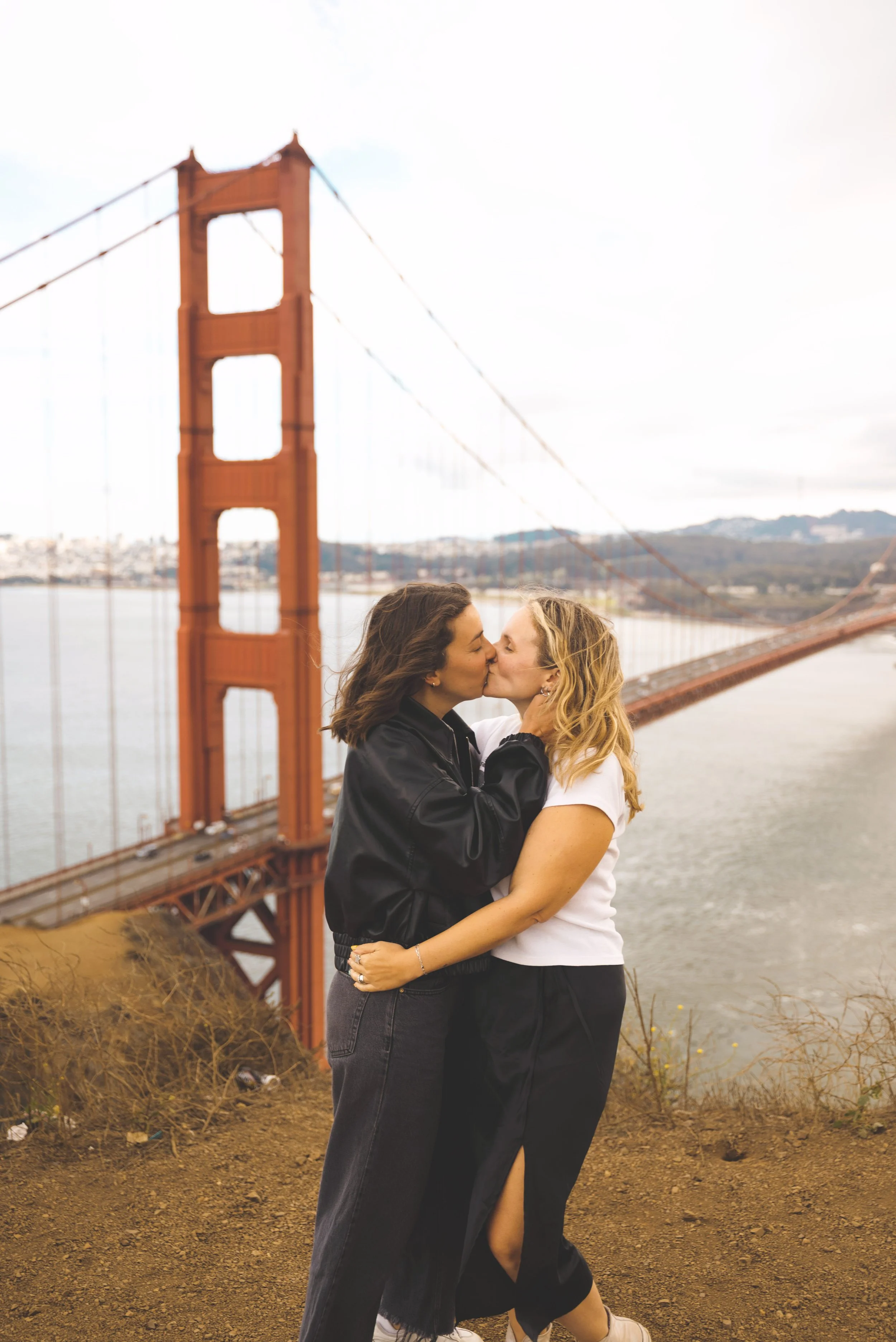two girls kissing in front of golden gate bridge