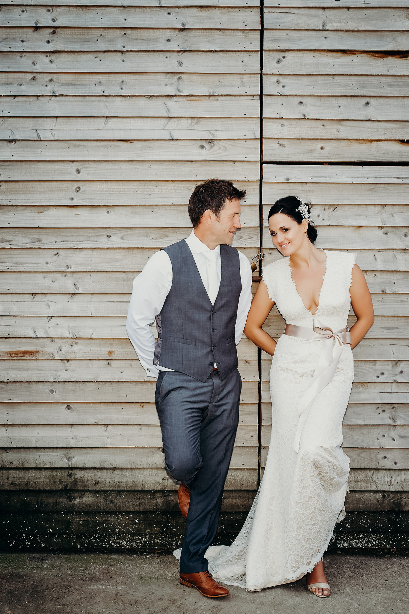 A bride and groom standing against a wooden fence, smiling at each other, on their wedding day in Llantwit, Bridgend. Shot by Jason Evans photography Bridgend