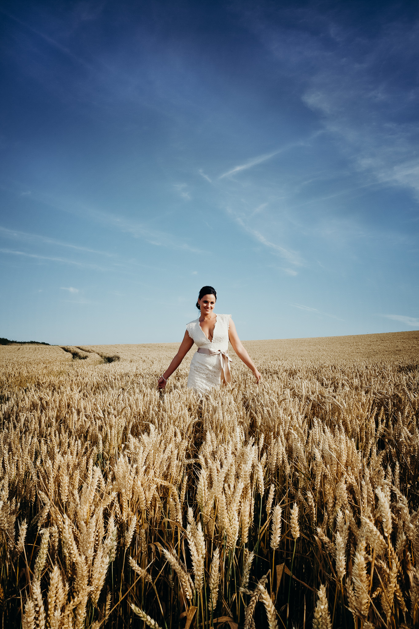 Woman in a wedding dress walking through a wheat field under a blue sky. Shot by Jason Evans photography Bridgend