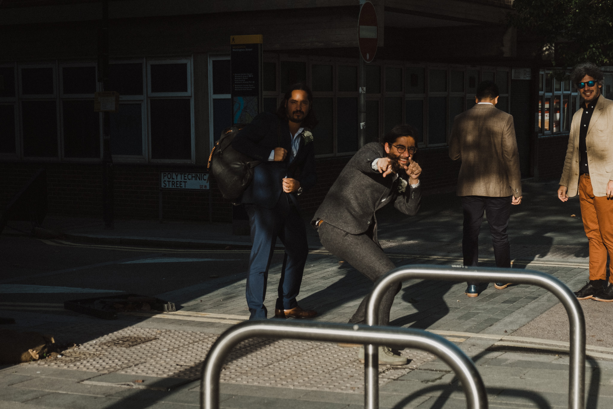 Four men in suits on city street with one pretending to shoot, another smiling, near a bus stop on Polytechnic Street. Shot by Jason Evans photography Bridgend