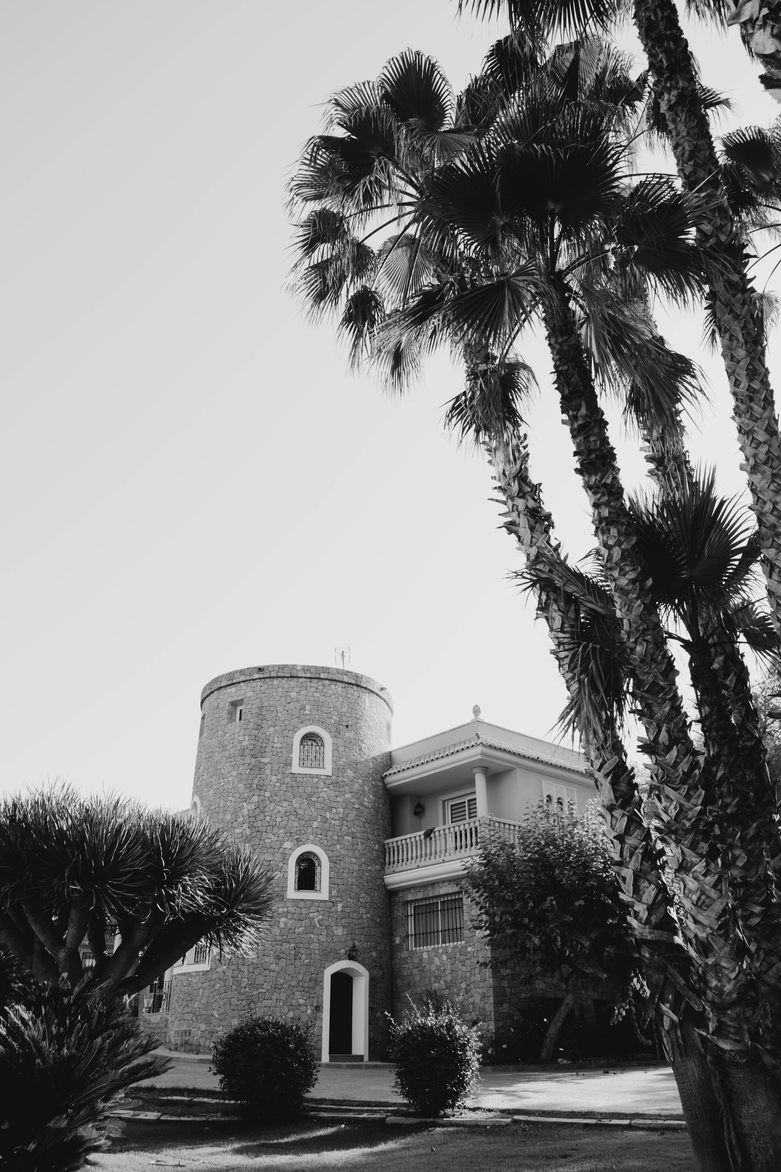 A stone house with a round tower and white accents, surrounded by palm trees and manicured bushes, under a clear sky in Ibiza. Shot by Jason Evans photography Bridgend