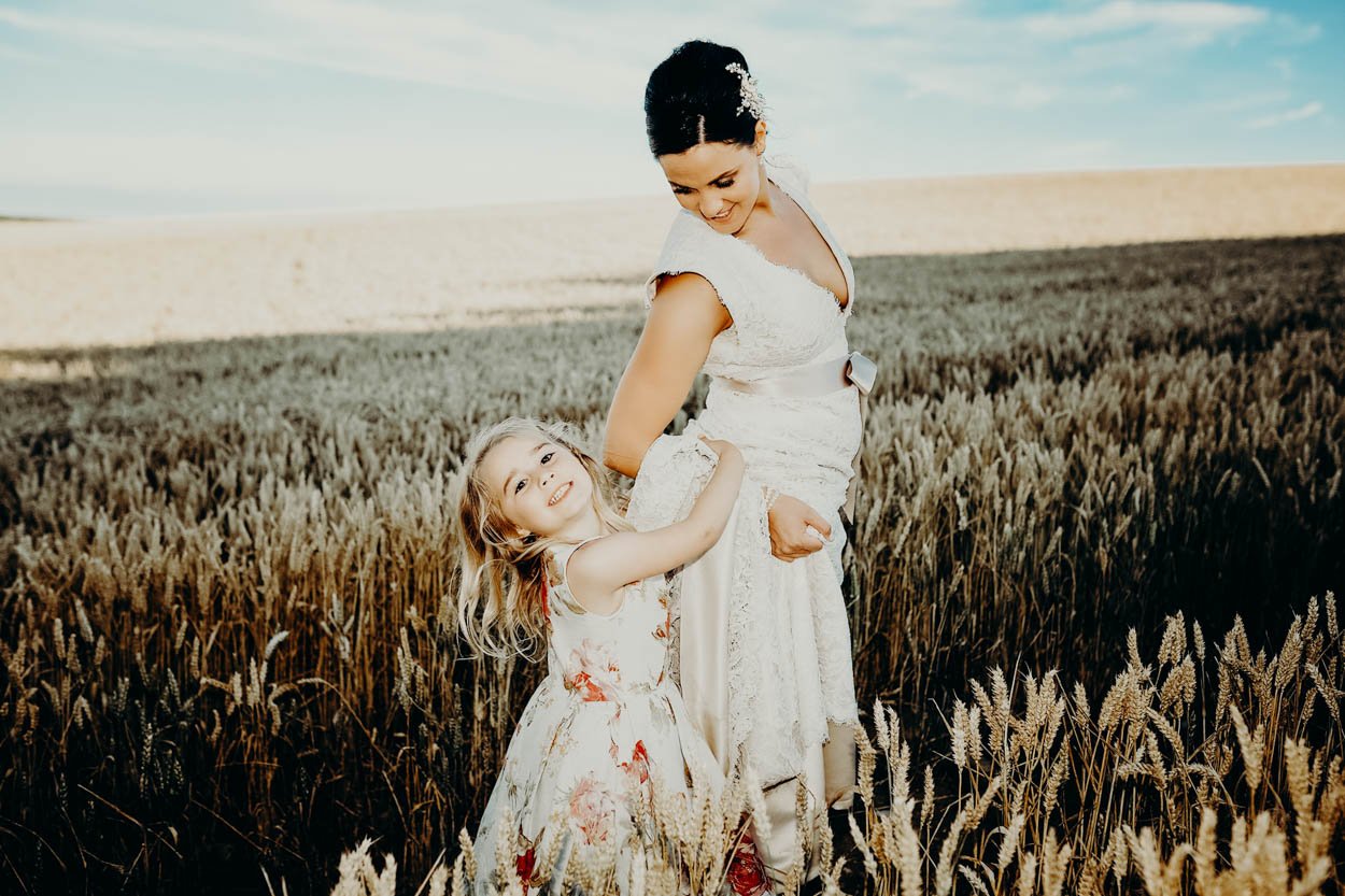 A bride in a white wedding dress and a young girl in a floral dress standing in a wheat field during daytime in bridgend, south wales. Shot by Jason Evans photography Bridgend